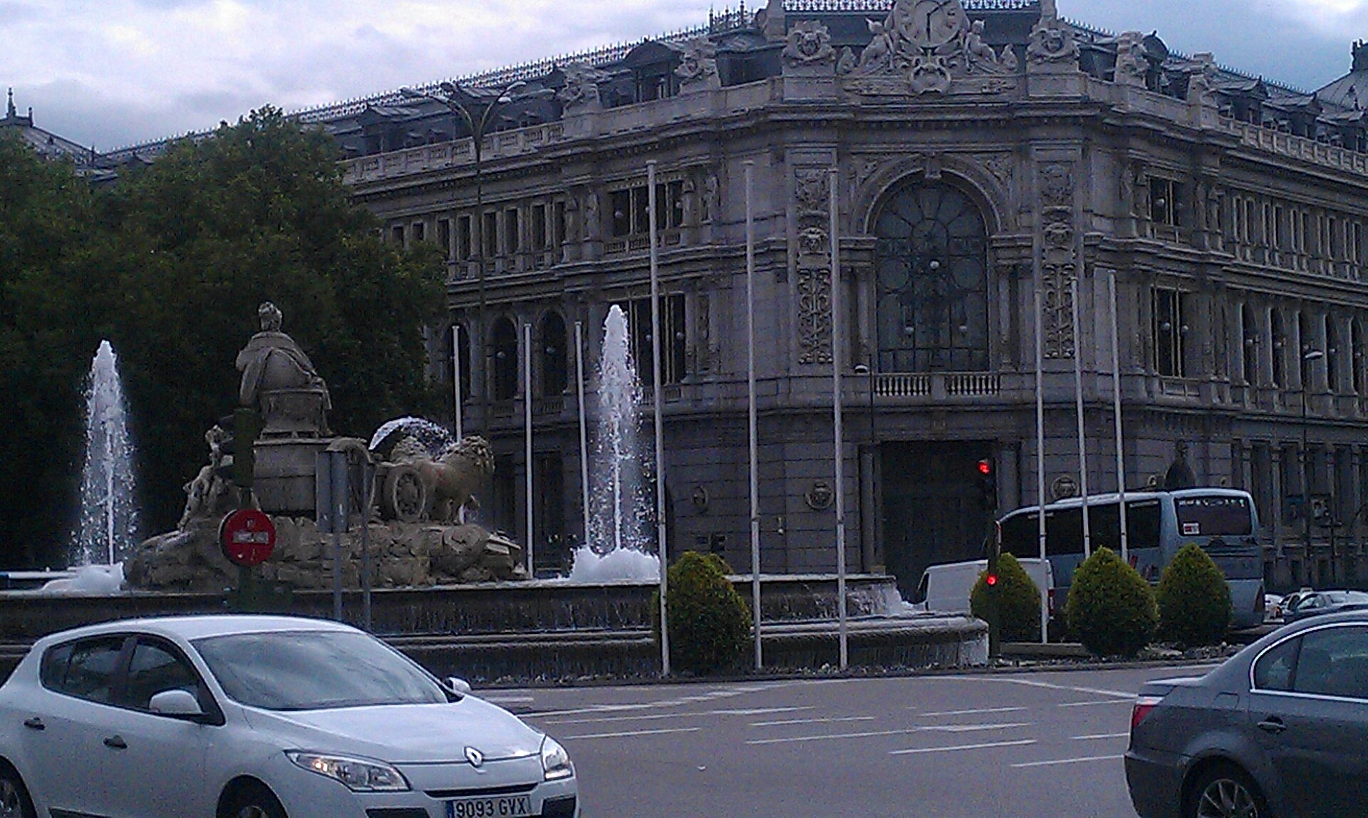 Edificio monumental junto a una fuente, con vehículos circulando por la vía.