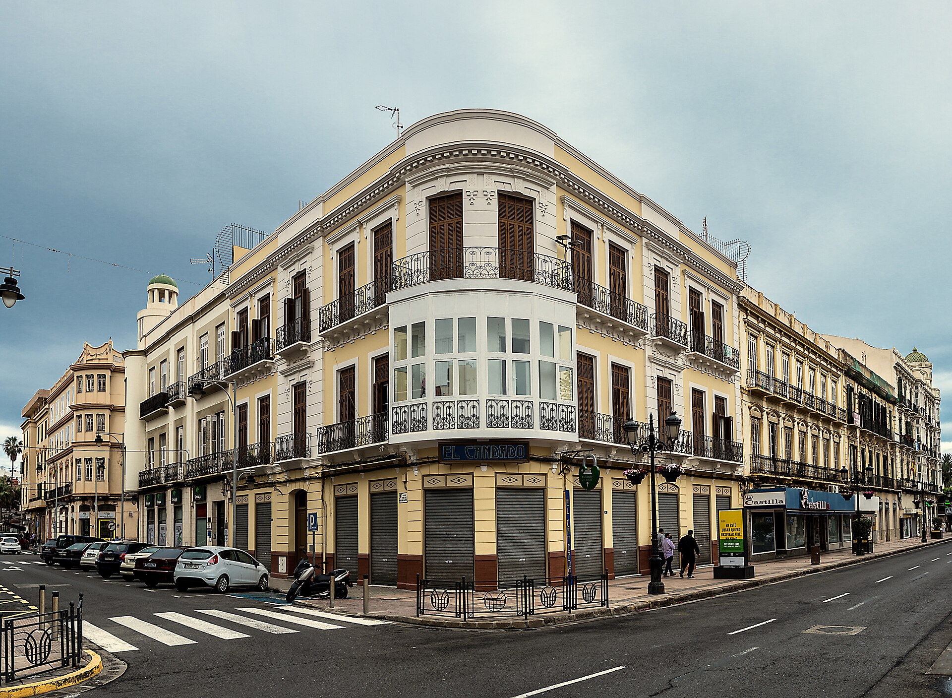 Edificio de varias plantas en una esquina, con balcones y comercios en la planta baja.