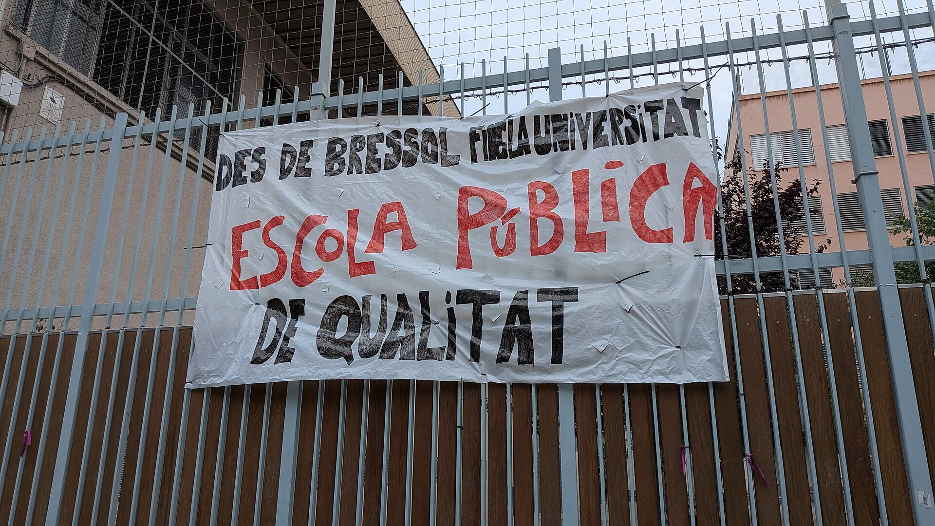 Una pancarta en una valla reclama una escuela pública de calidad desde la educación infantil hasta la universidad.