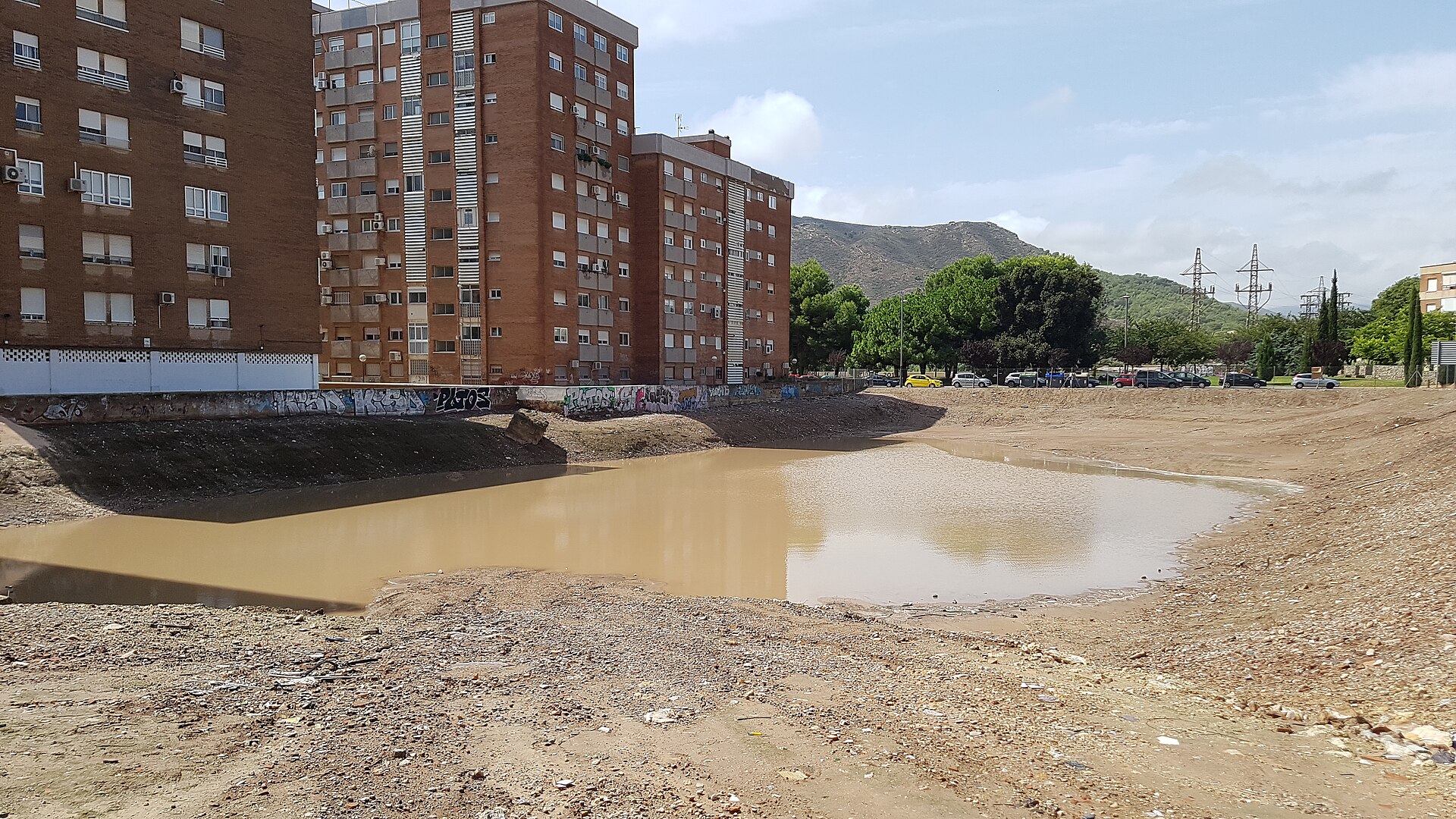 Solar con una gran acumulación de agua embarrada frente a varios bloques de viviendas.