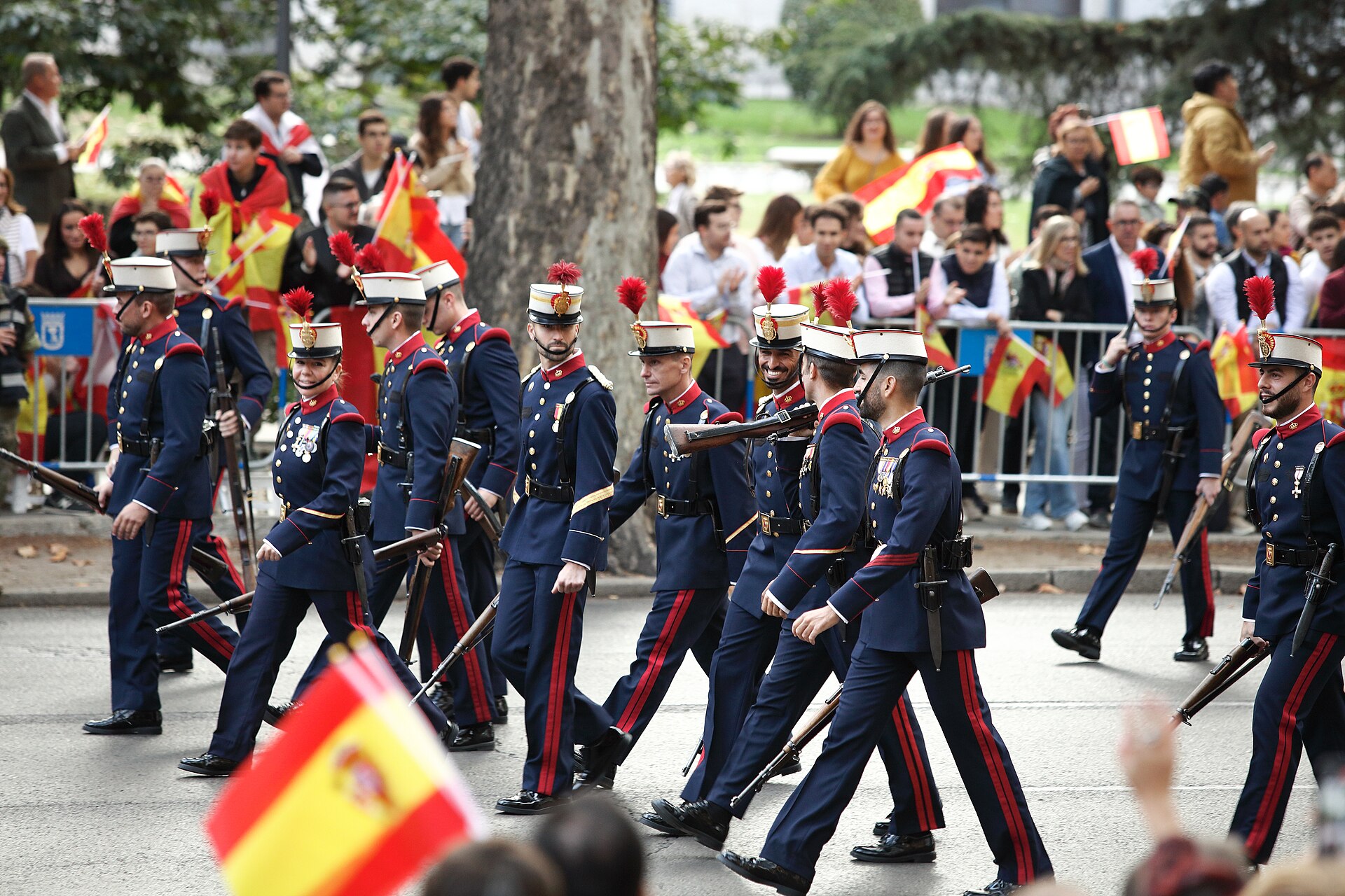 Un grupo de militares con uniforme de gala y fusiles marcha por una avenida.