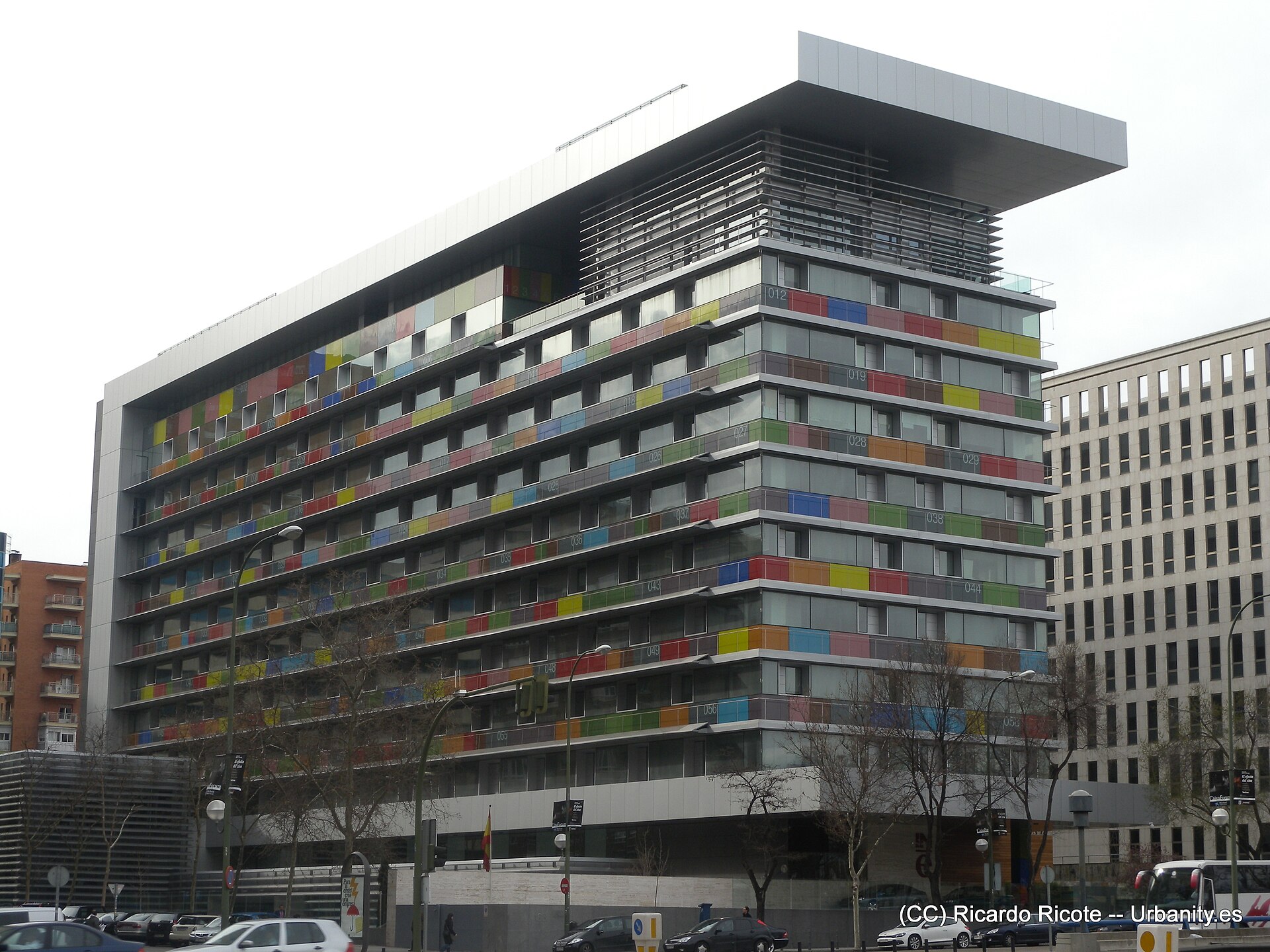 Vista exterior de un edificio de varias plantas, con fachadas acristaladas y paneles de colores.