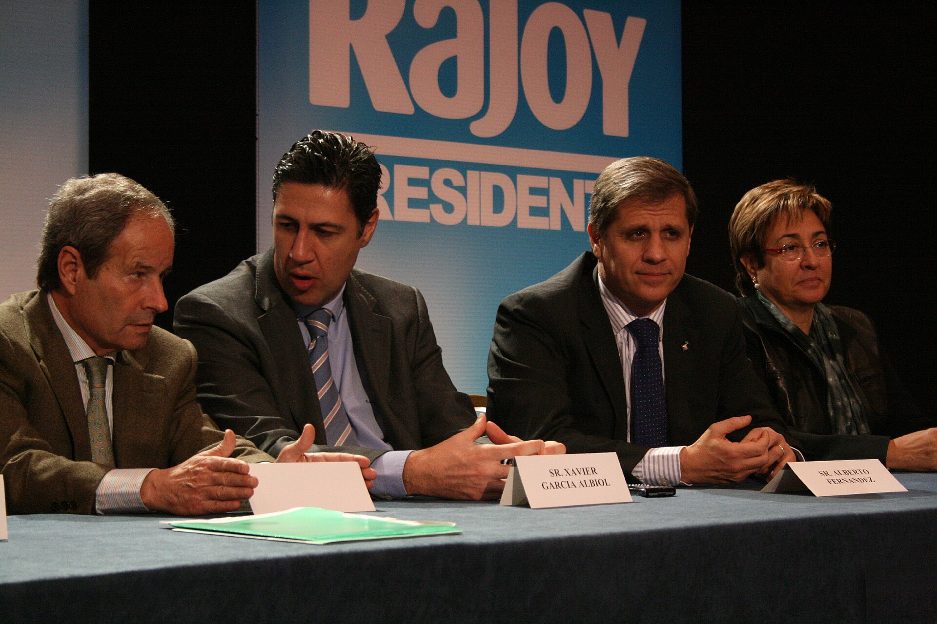 Varias personas sentadas en una mesa de debate, con carteles al fondo.