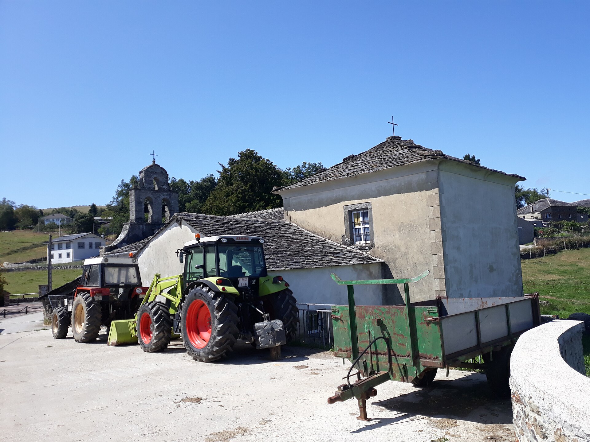 Dos tractores agrícolas y un remolque están estacionados junto a una iglesia.