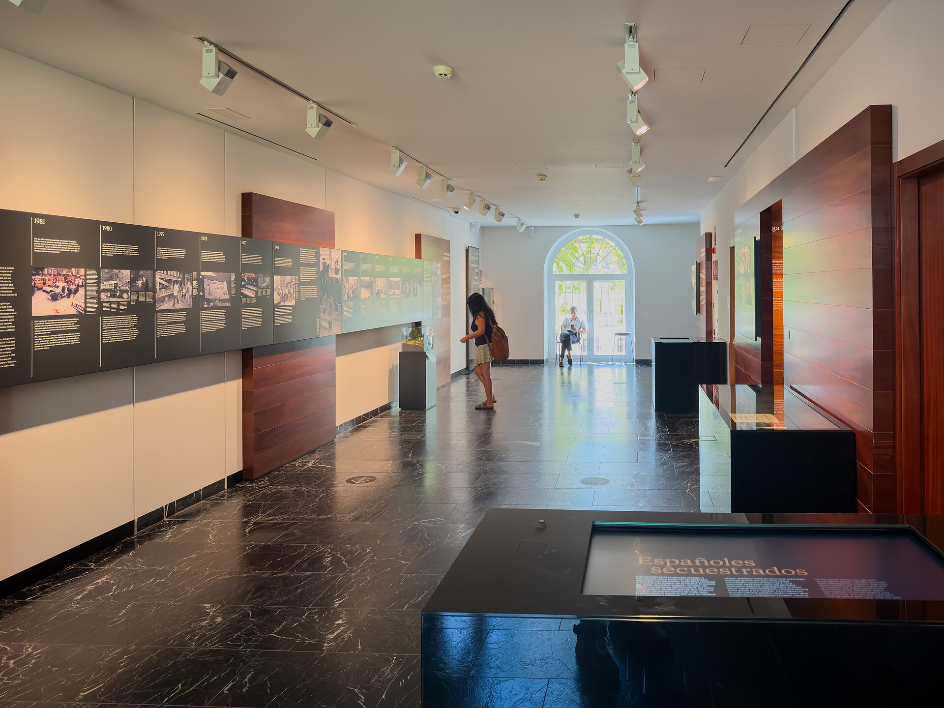 Paneles cronológicos con fotografías y textos ocupan una sala de exposición; una visitante se detiene a leer.