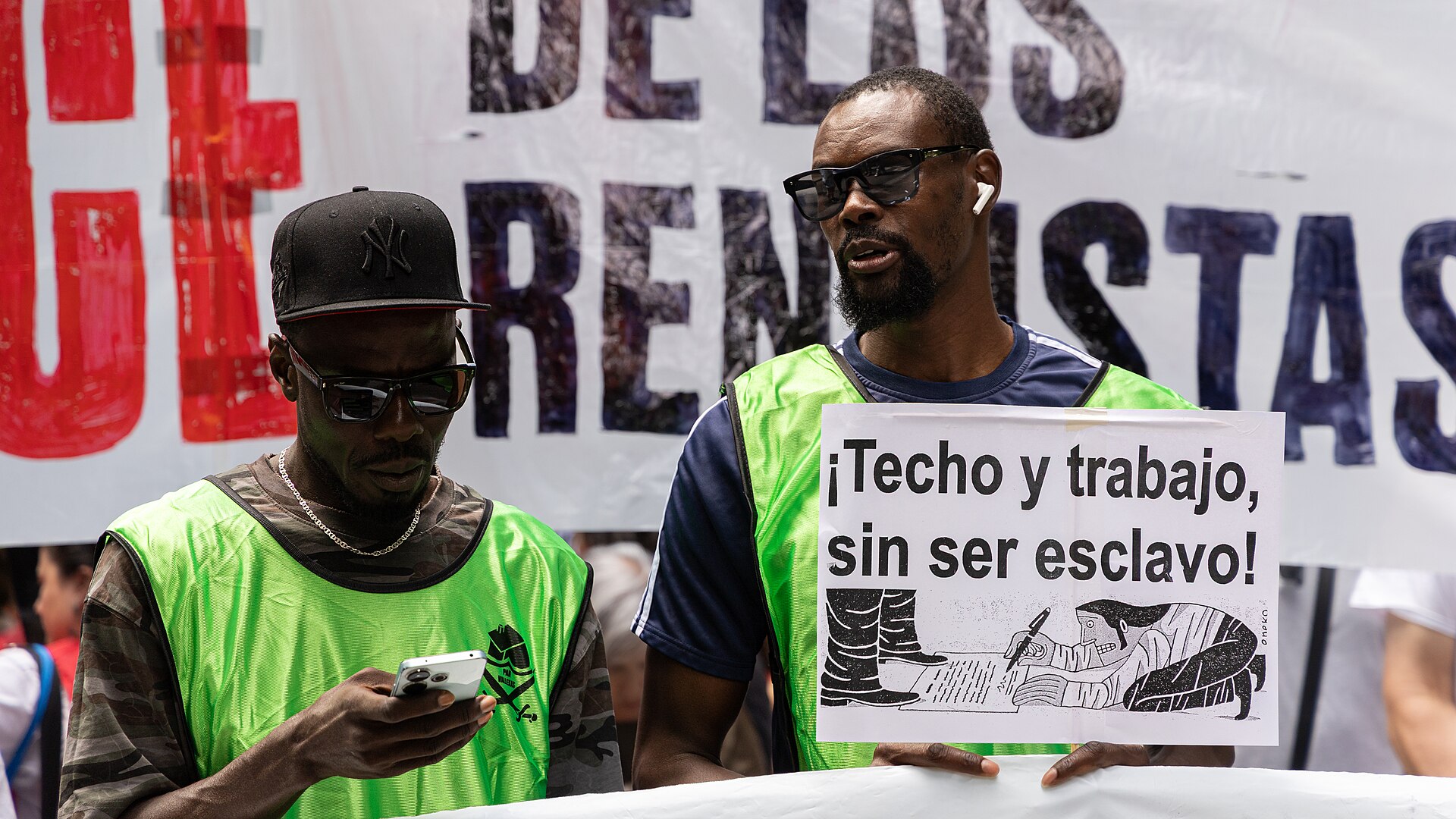 Dos manifestantes muestran un cartel con el lema «¡Techo y trabajo, sin ser esclavo!».