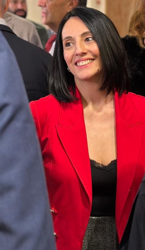 Una mujer con chaqueta roja sonríe entre varias personas.