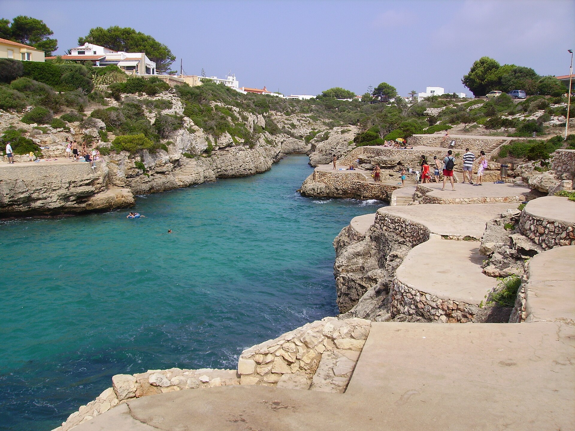 Una cala rocosa con plataformas junto al agua y bañistas.