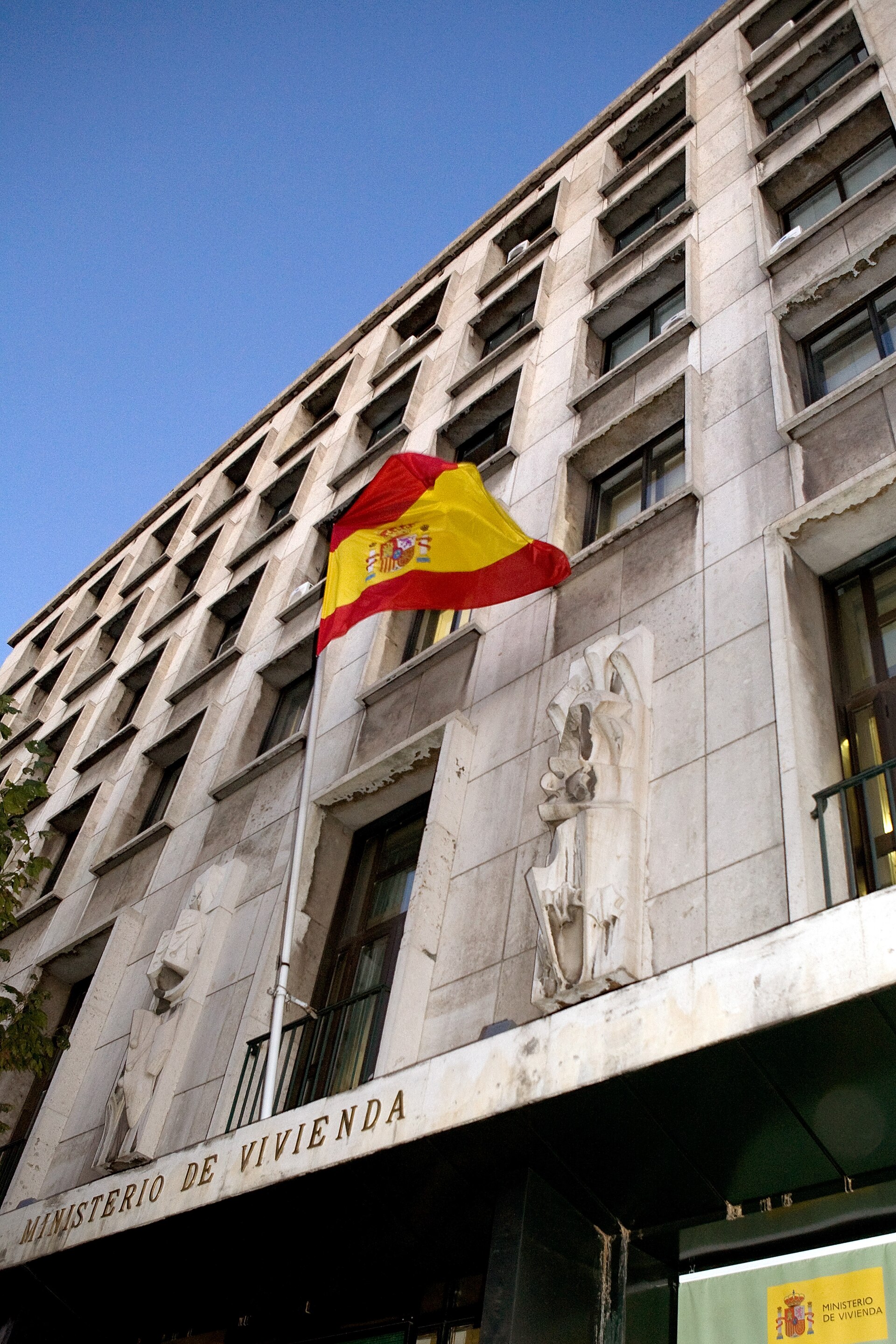 Fachada institucional con bandera española y rótulo del Ministerio de Vivienda.