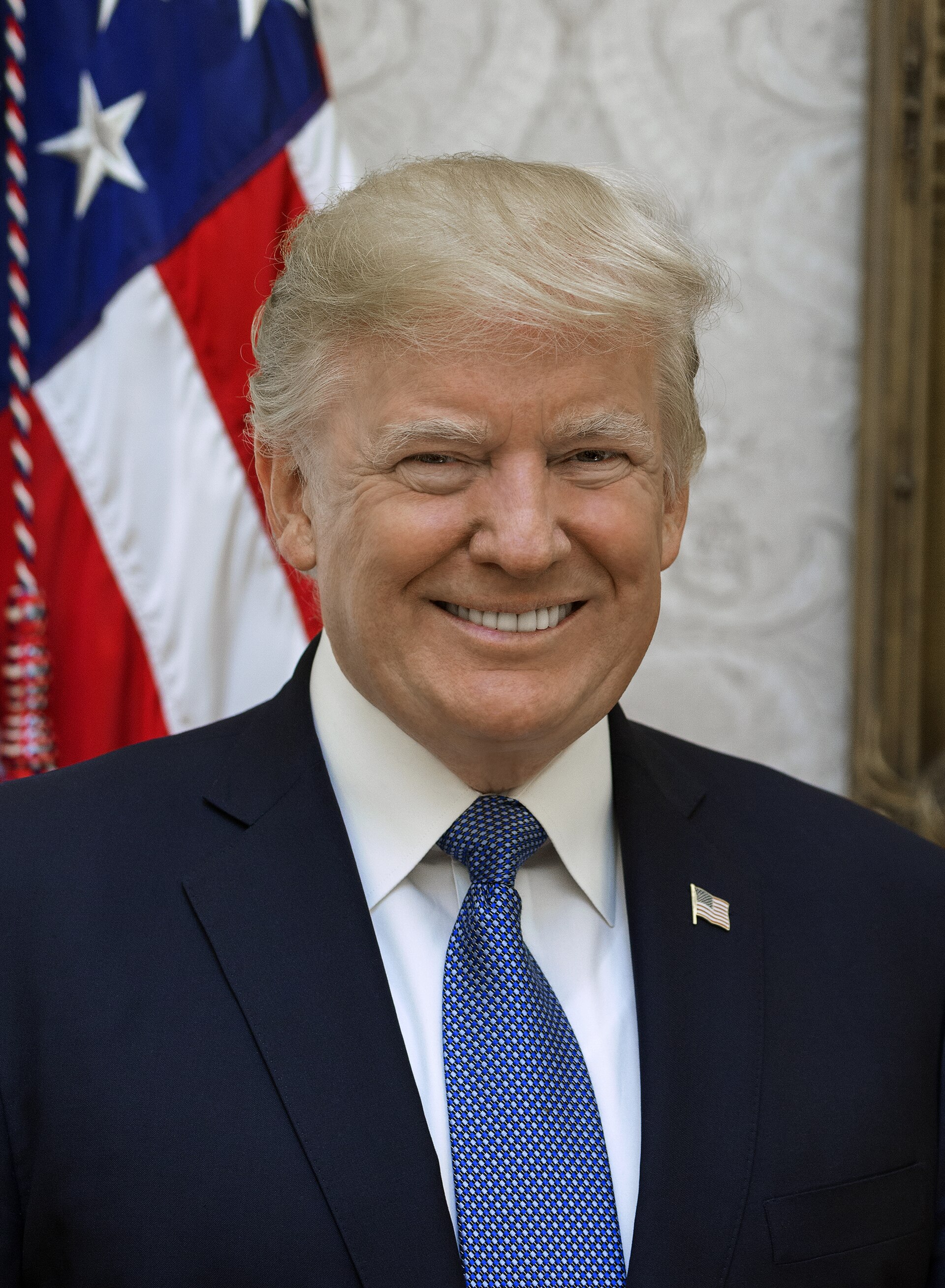 Retrato de un hombre sonriente con traje y corbata, ante una bandera de Estados Unidos.