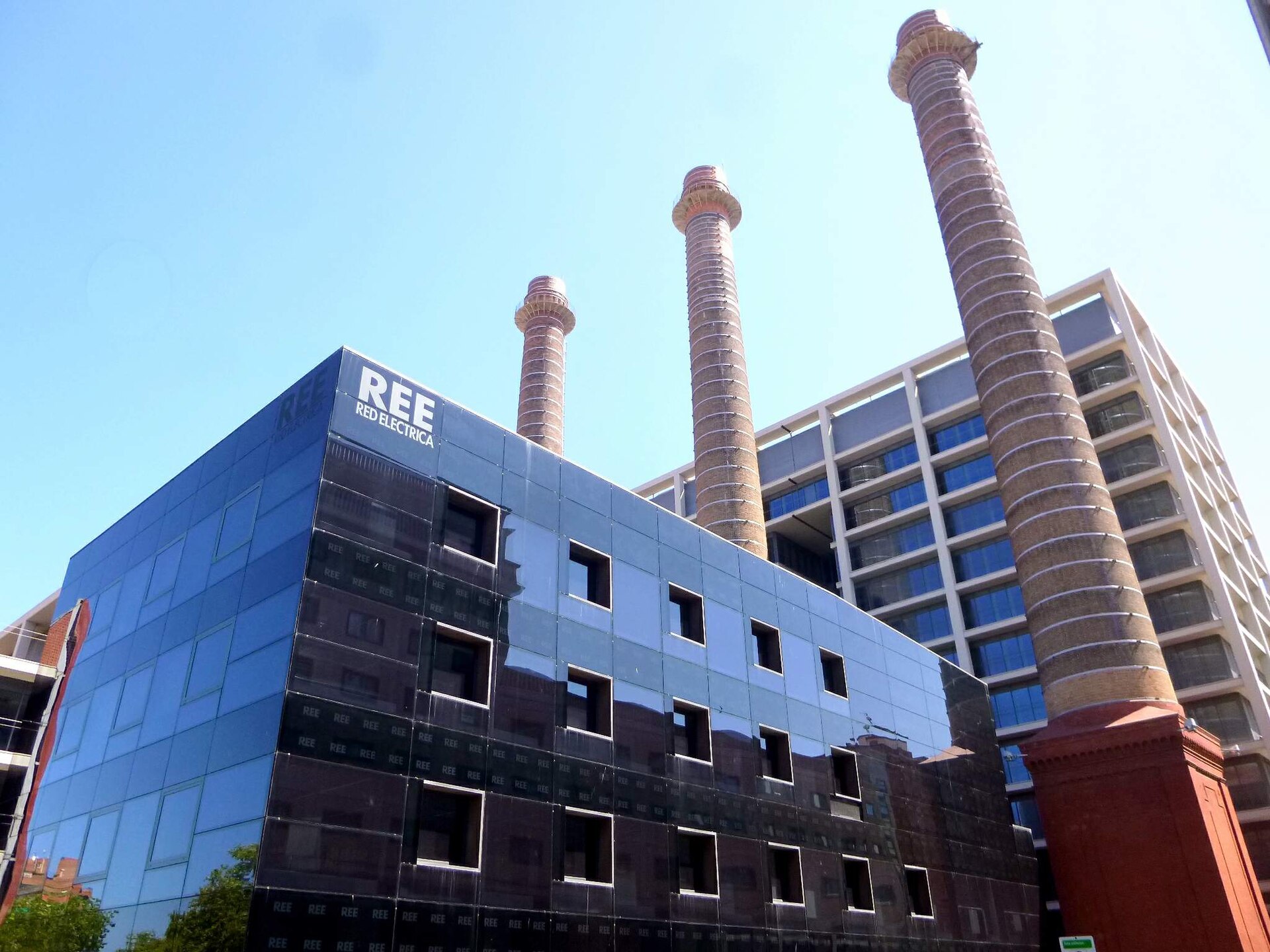 Fachada de un edificio con el rótulo «REE Red Eléctrica» y varias chimeneas.