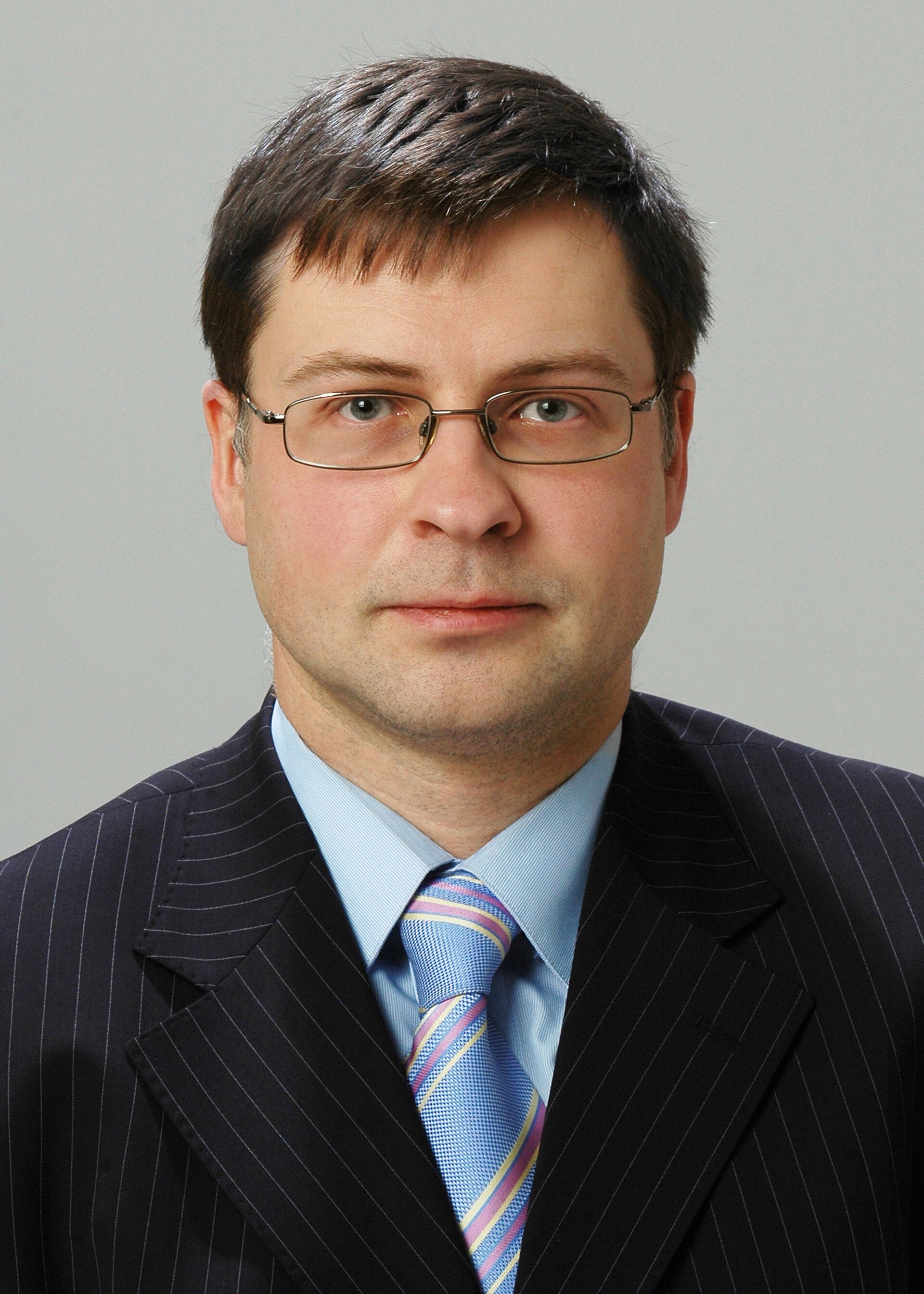 Retrato de un hombre con gafas, traje oscuro y corbata a rayas.