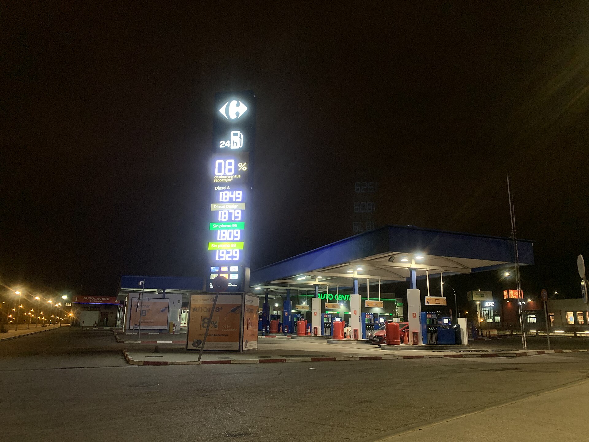 Gasolinera iluminada de noche, con un panel que muestra precios de distintos combustibles.