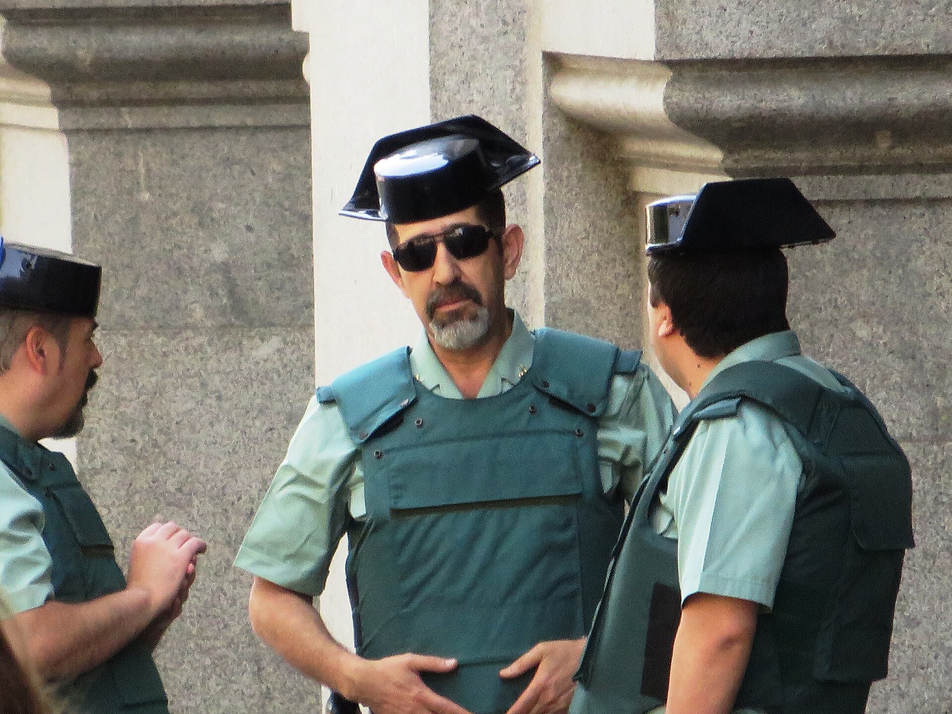 Tres agentes uniformados conversan bajo una estructura de piedra.