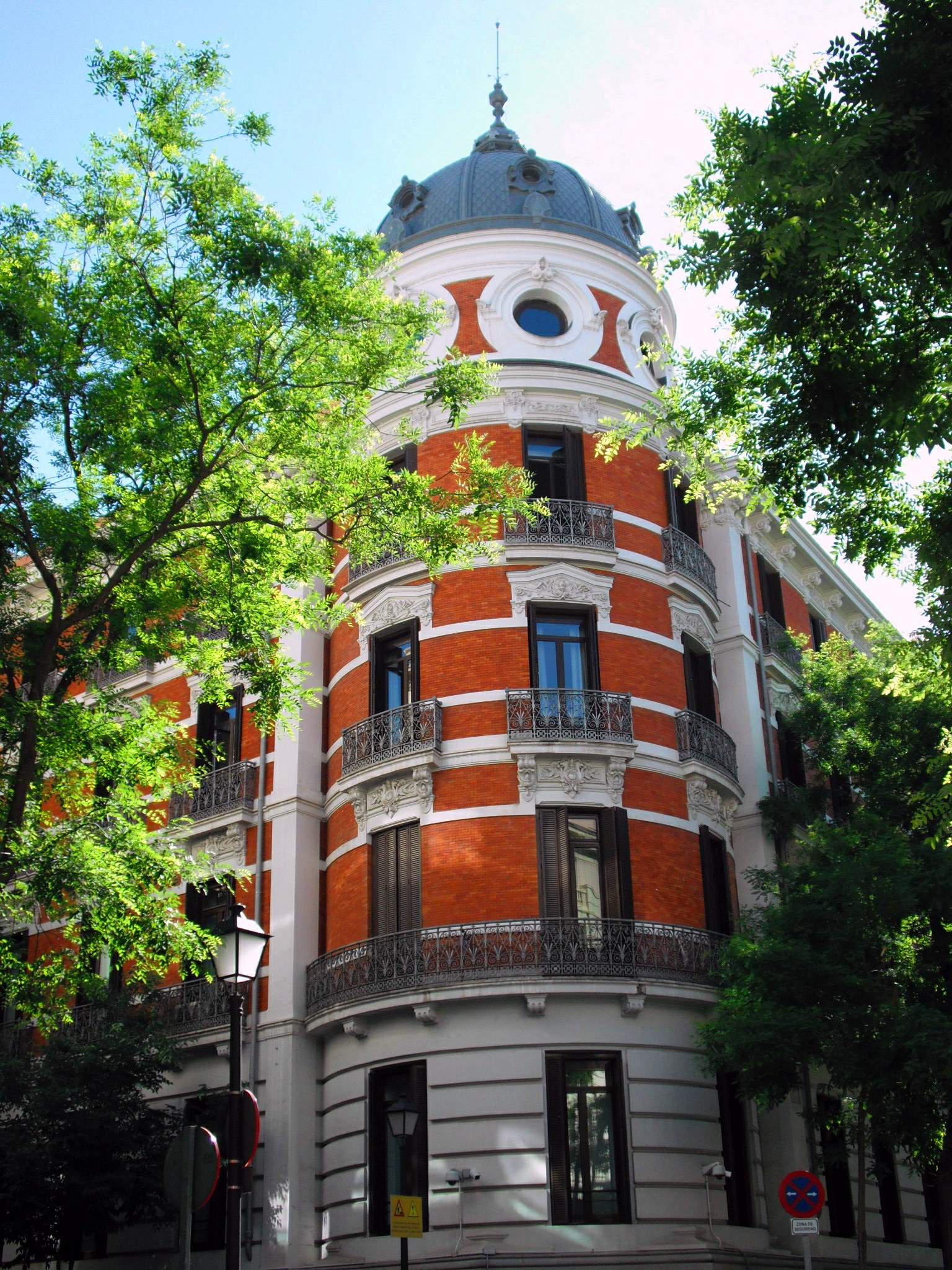 Fachada ornamentada de un edificio institucional, parcialmente cubierta por árboles.