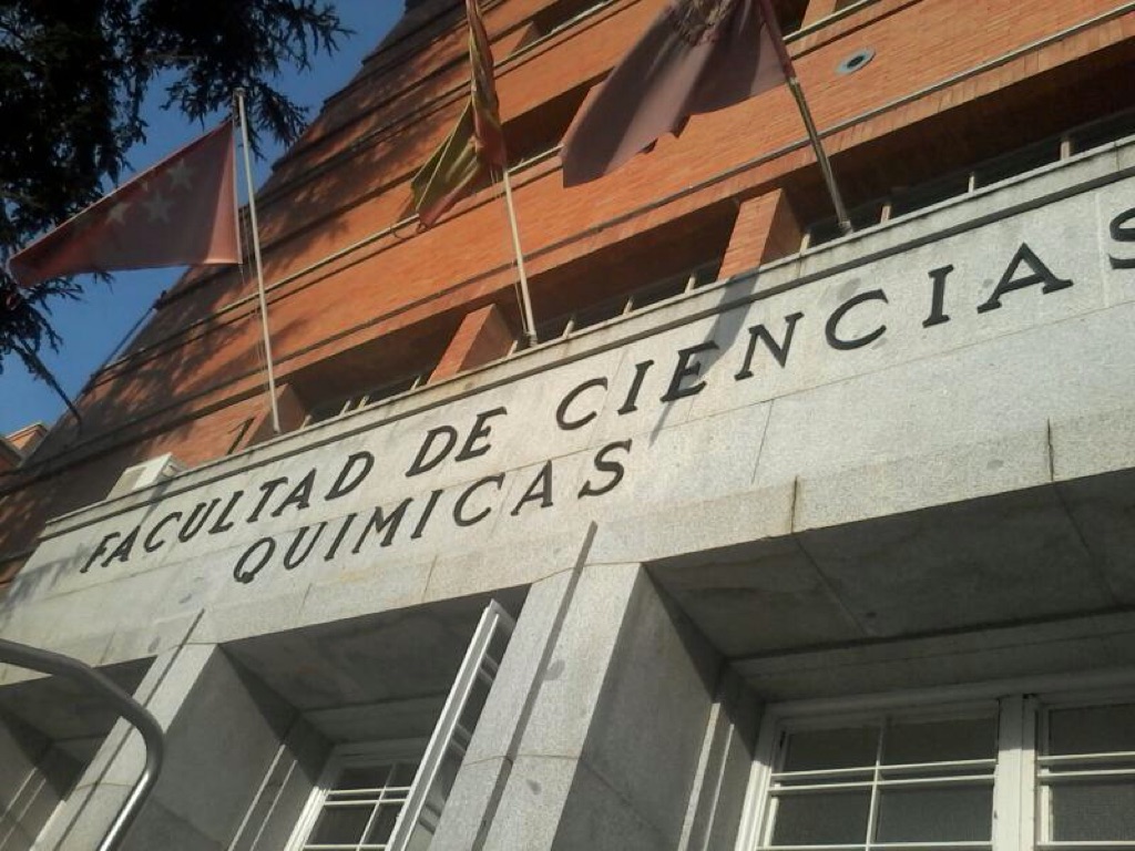 Rótulo de una facultad en la fachada de un edificio, junto a varias banderas.