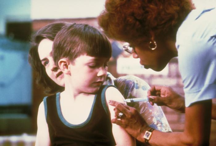 Un niño recibe una inyección en el brazo mientras una profesional sanitaria se la administra.
