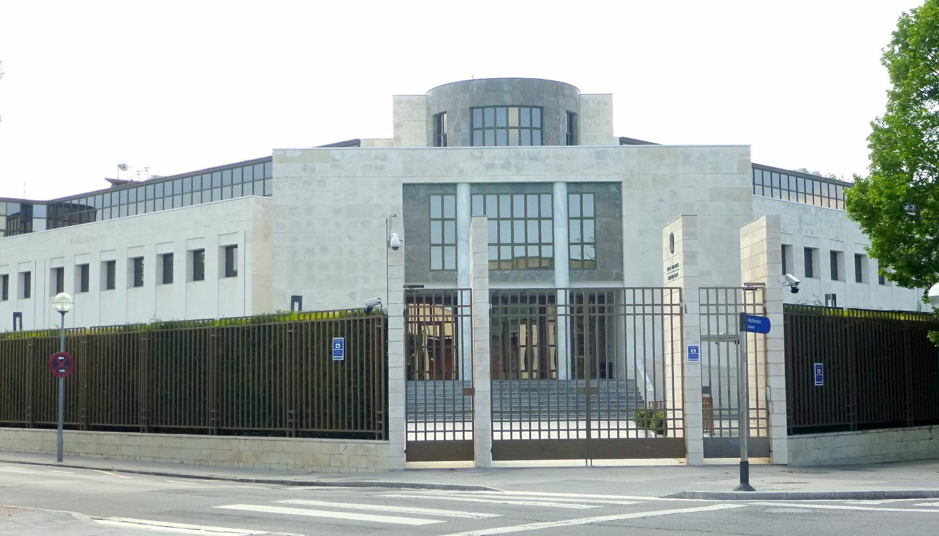 Fachada de un edificio institucional de piedra clara, con ventanas y una entrada vallada.