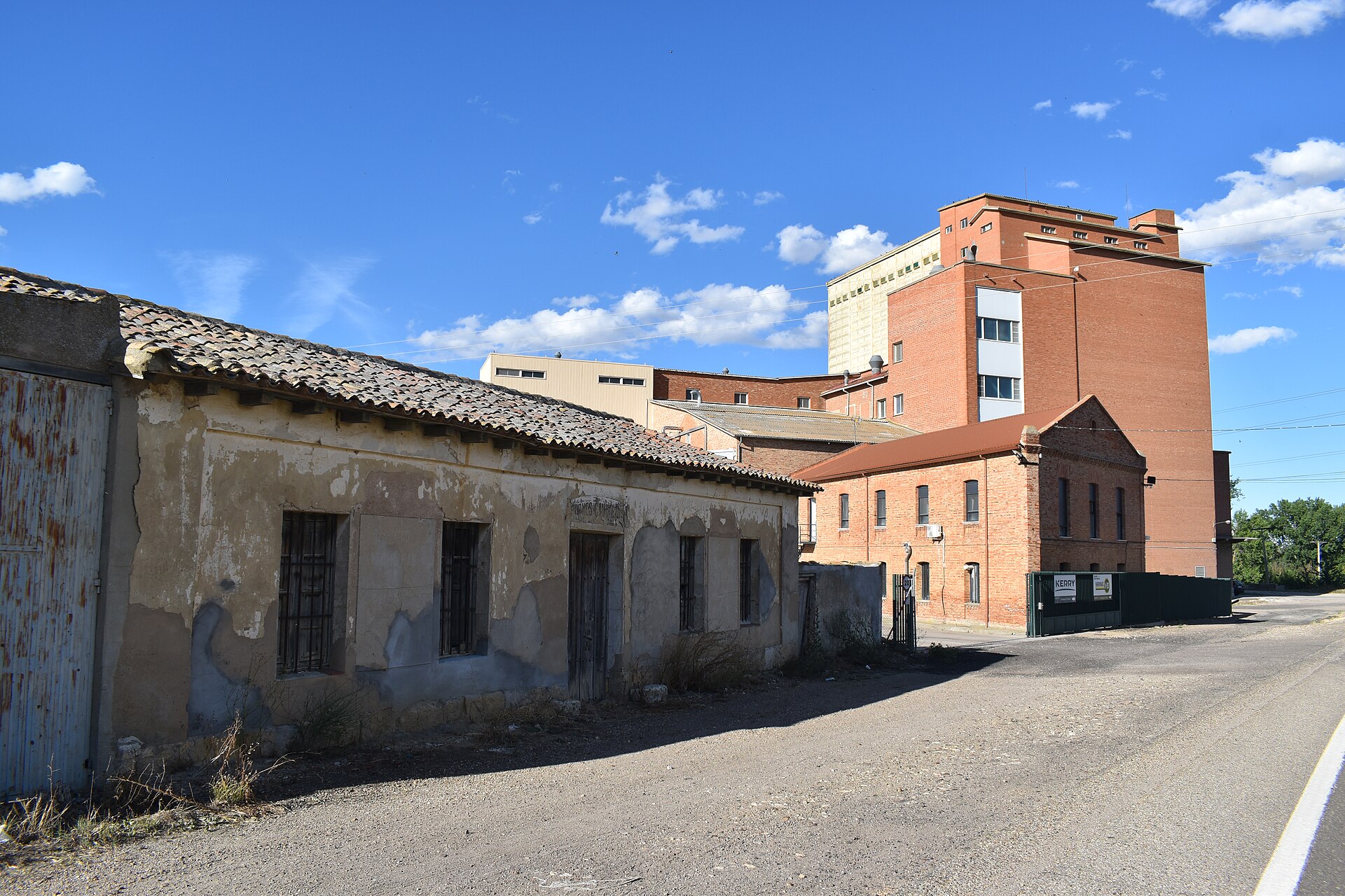 Un edificio antiguo junto a una construcción industrial de ladrillo, vistos desde una carretera.
