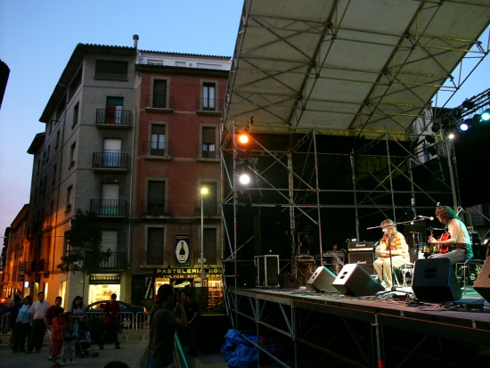 Dos músicos actúan en un escenario al aire libre junto a varios edificios.