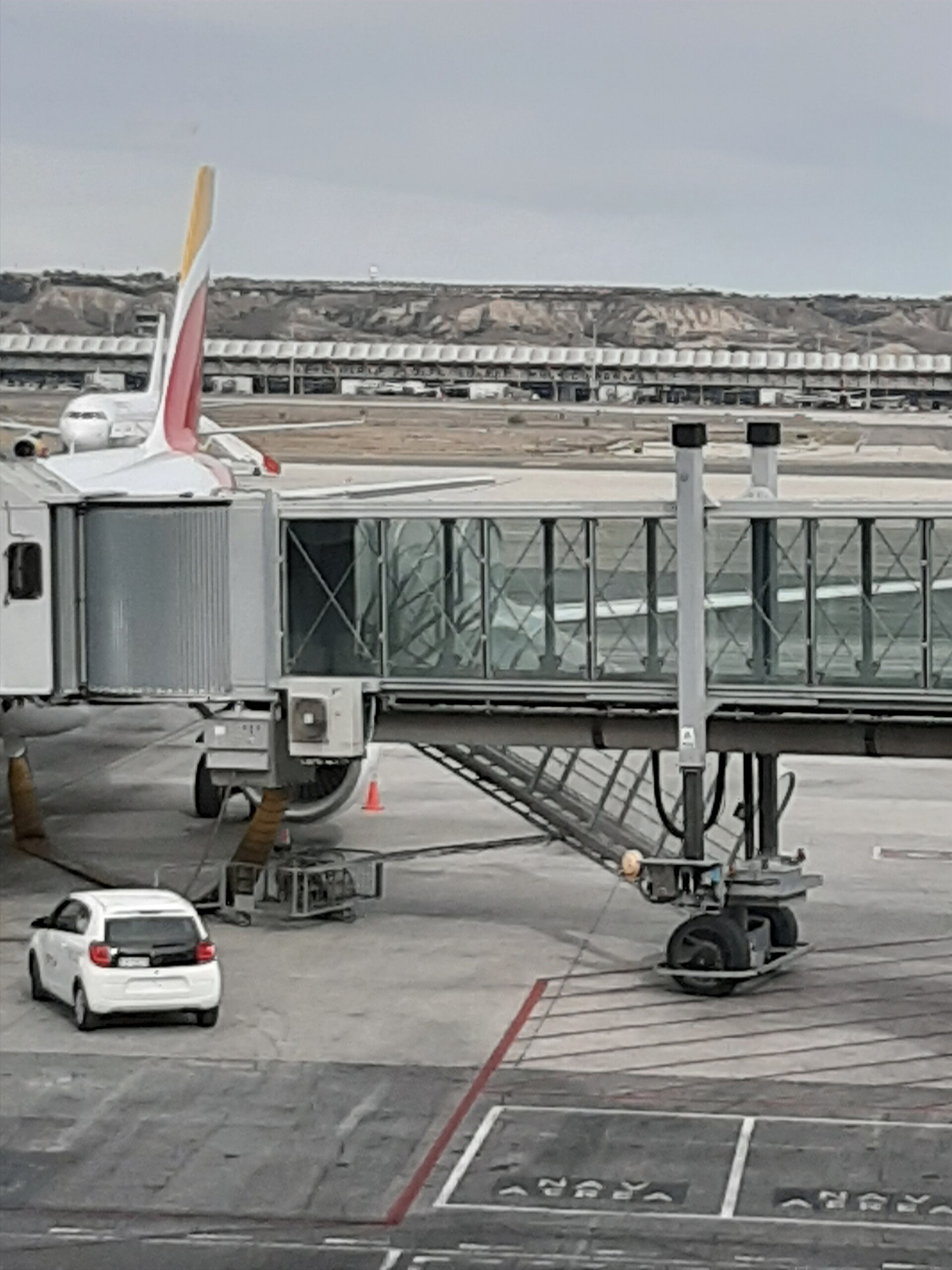 Un avión estacionado junto a una pasarela de embarque; al fondo se ven otras aeronaves y parte de la terminal.