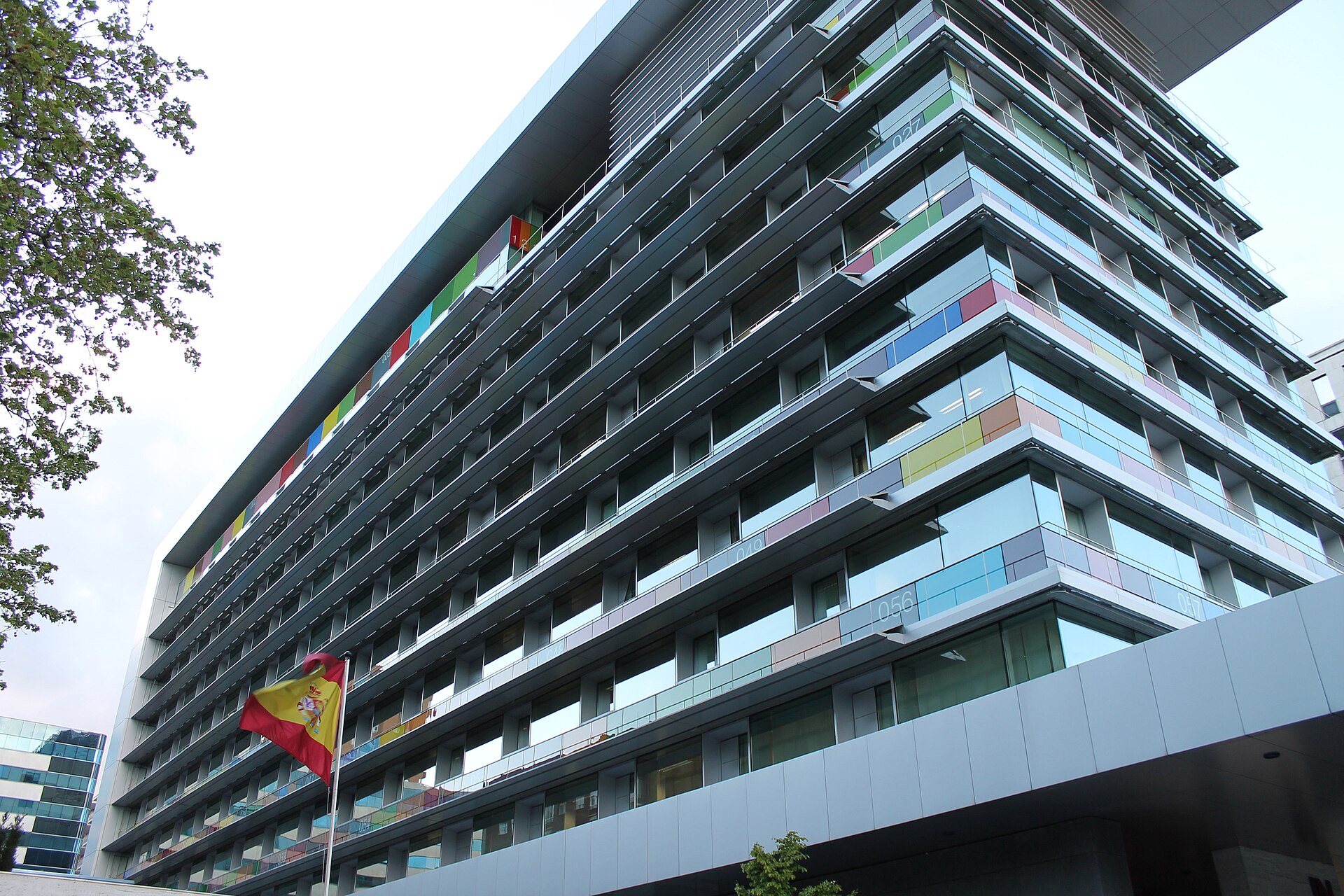 Edificio de oficinas visto desde abajo, con una bandera de España en primer plano.