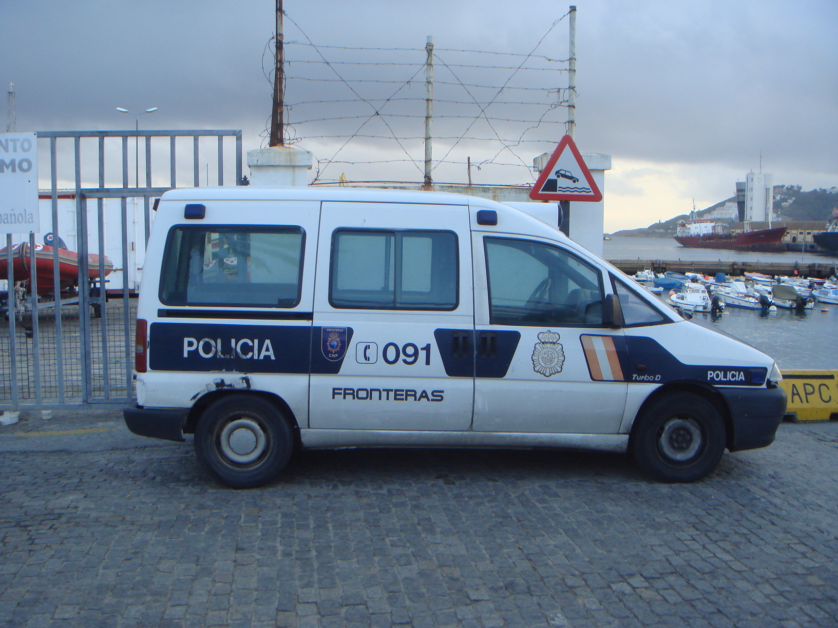 Una furgoneta policial con la inscripción «Fronteras», estacionada junto a una zona portuaria.