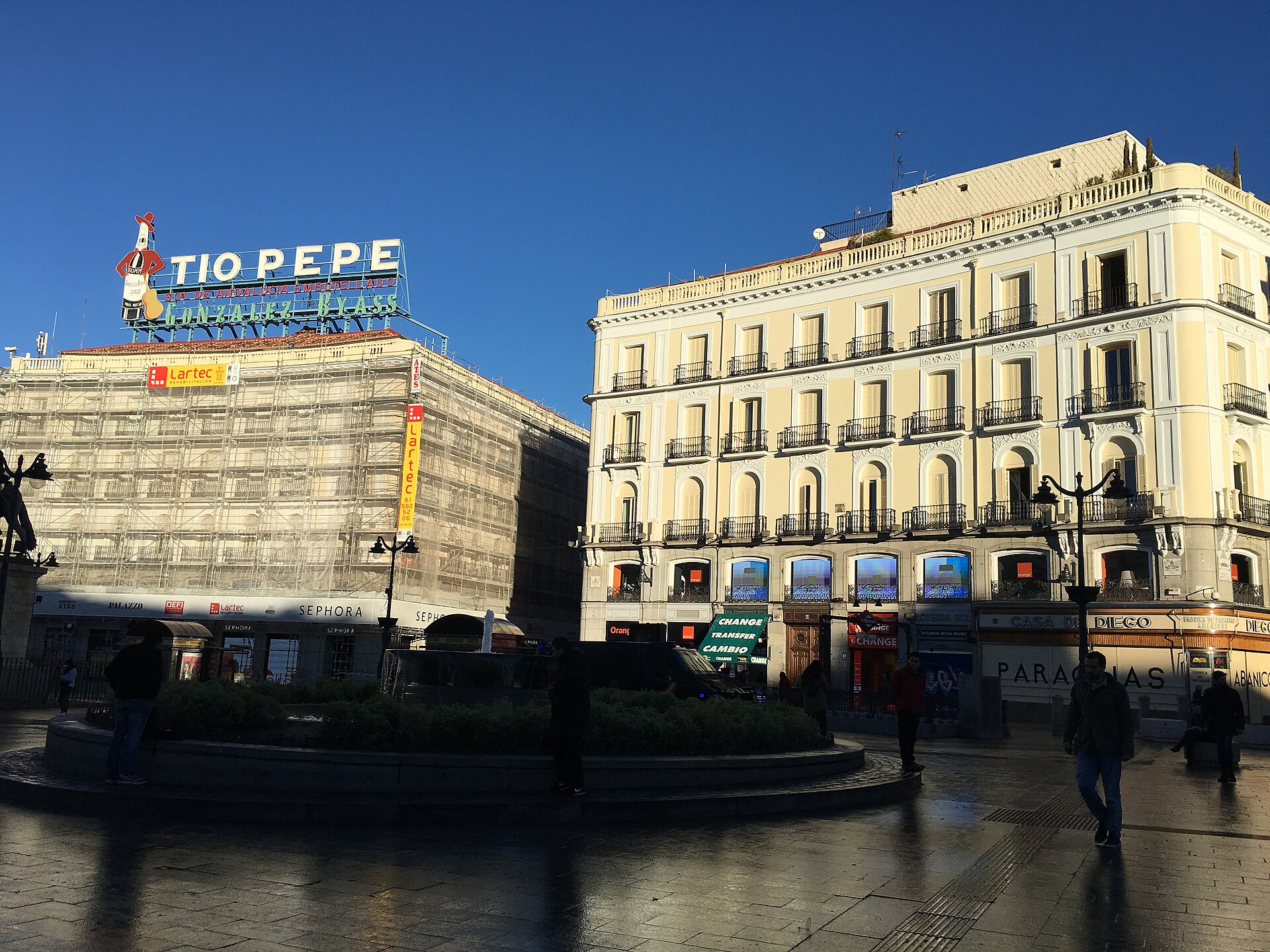 Fachadas de varios pisos y una plaza peatonal, con un gran rótulo luminoso sobre uno de los edificios.