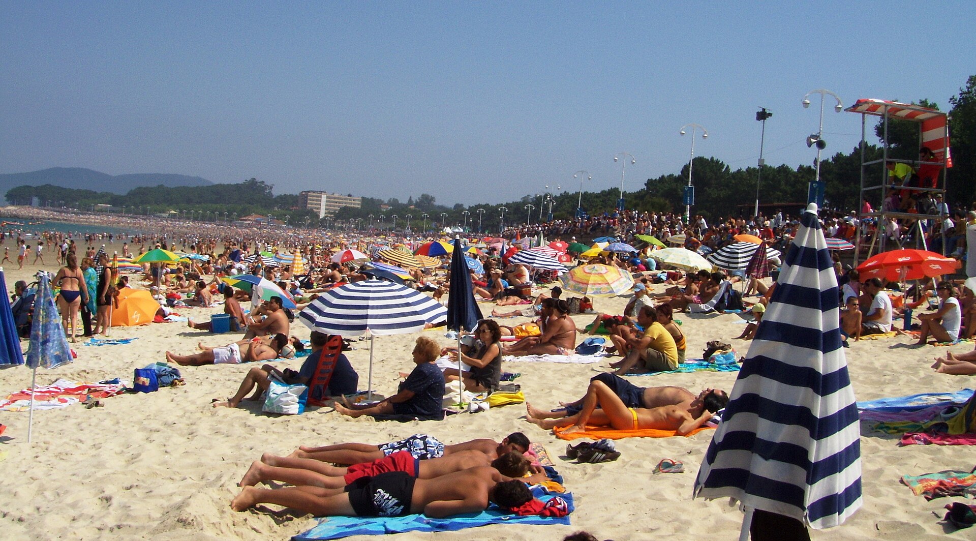 Una playa abarrotada de bañistas y sombrillas bajo un cielo despejado.