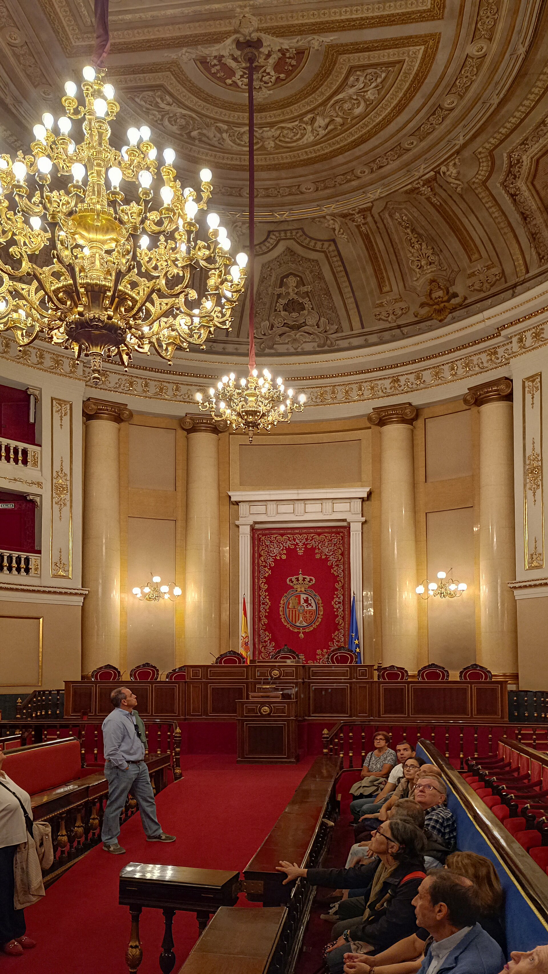 Sala ornamentada con bancos y varias personas sentadas.