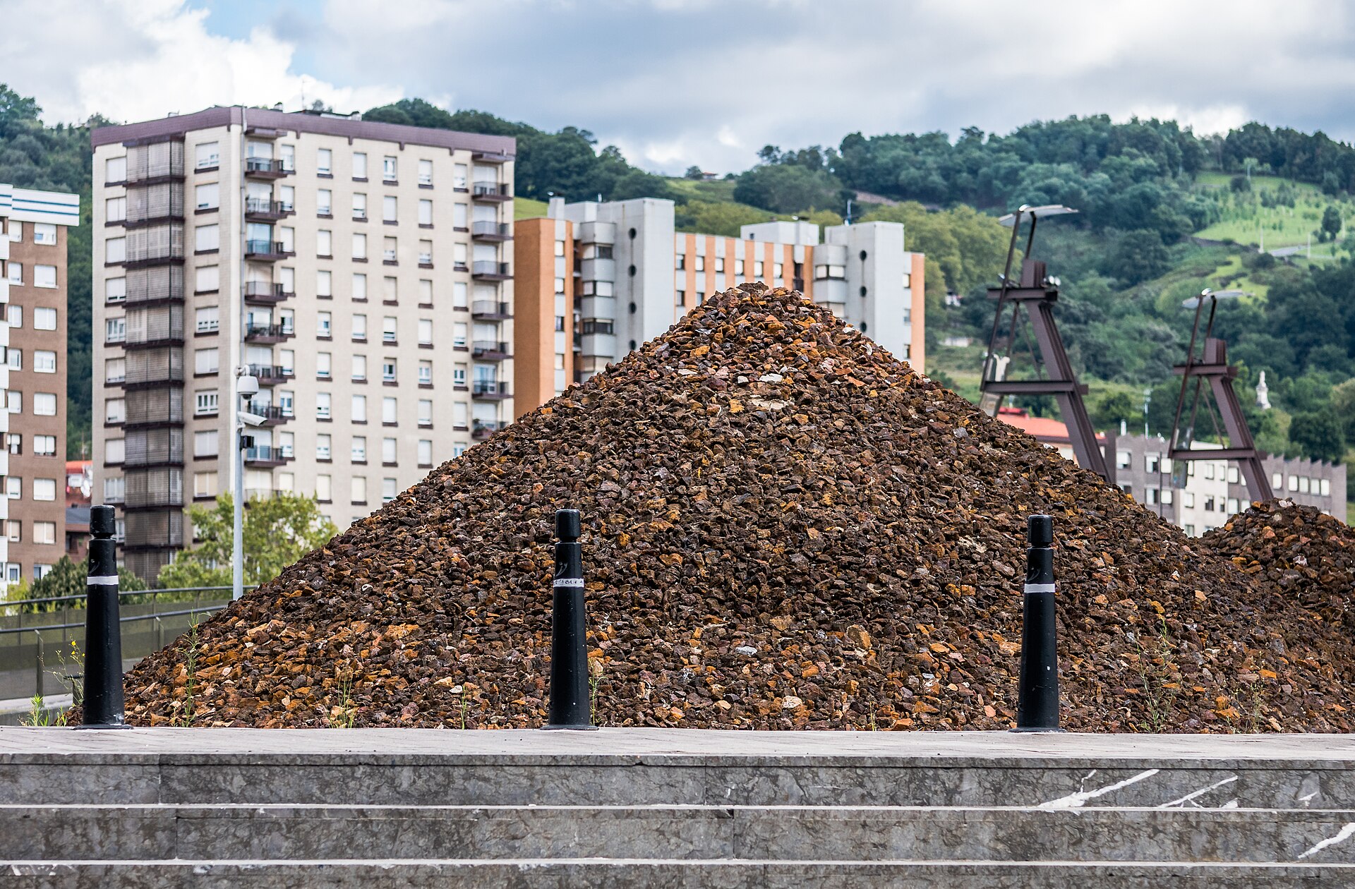 Montículo de mineral frente a varios bloques residenciales y una ladera arbolada.