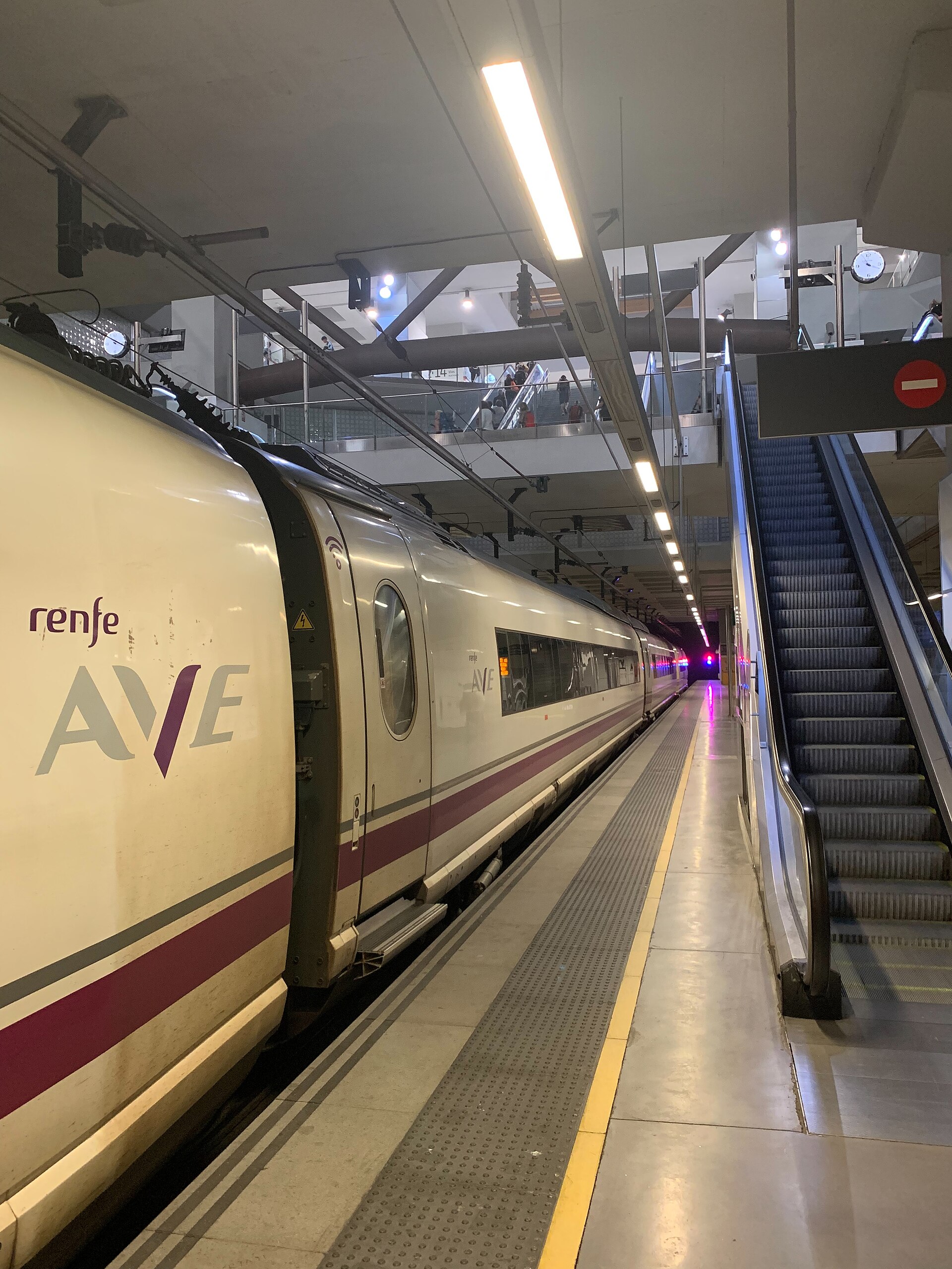 Un tren con el rótulo AVE ocupa una vía junto al andén y unas escaleras mecánicas.