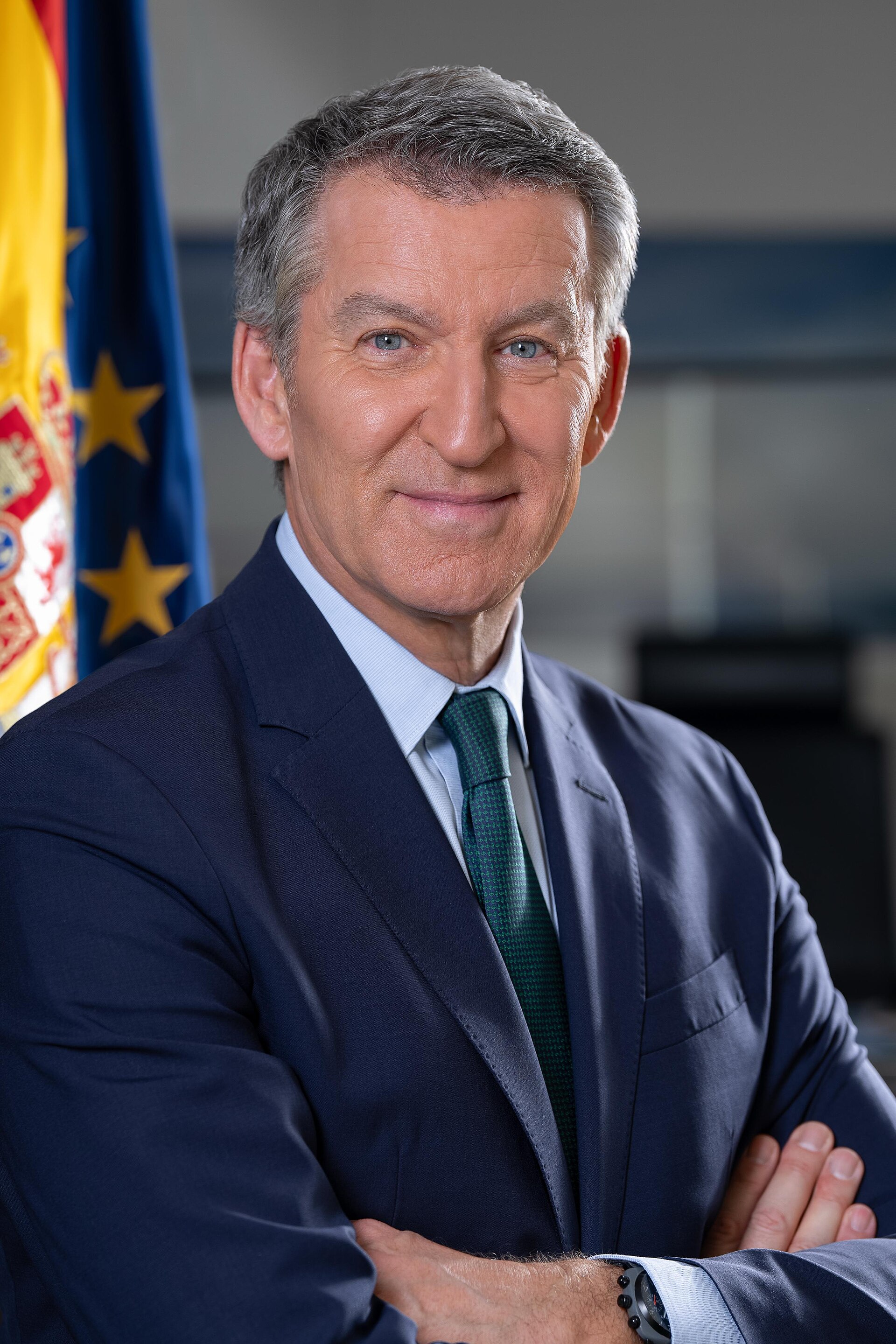 Un hombre con traje posa con los brazos cruzados ante las banderas de España y la Unión Europea.