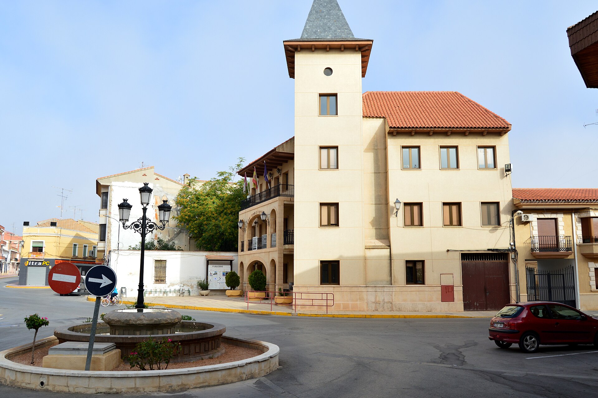 Edificio con torre y soportales en una plaza, junto a una fuente.