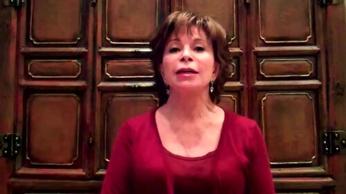 Una mujer habla ante una puerta de madera con paneles tallados.