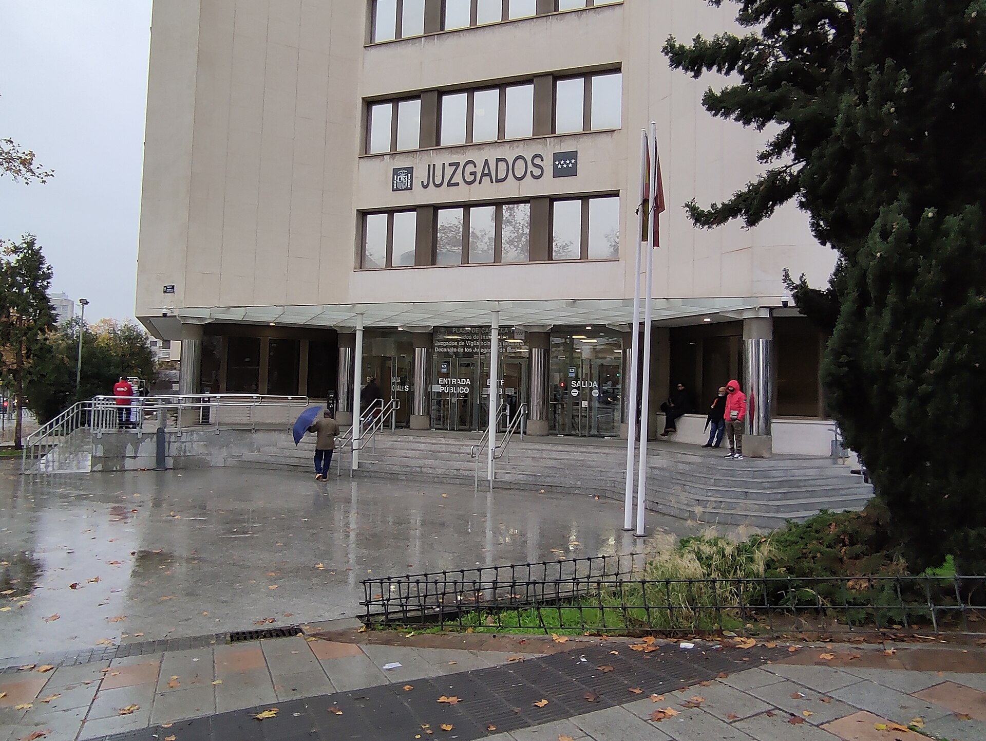 Entrada de un edificio con el rótulo «Juzgados», banderas y varias personas.