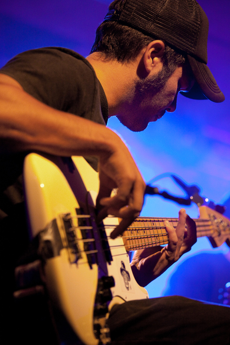 Músico tocando un instrumento de cuerda eléctrica bajo luces de escenario.
