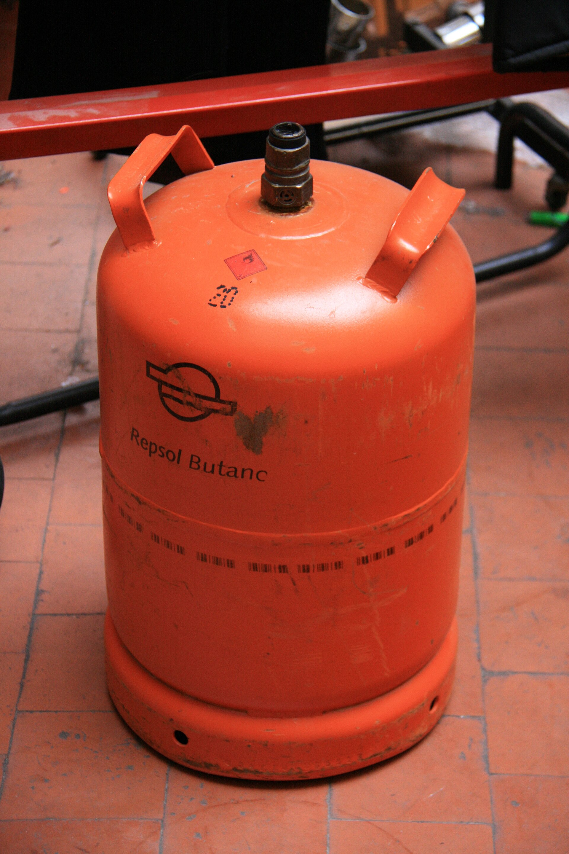 Una bombona naranja de butano sobre un suelo de baldosas.