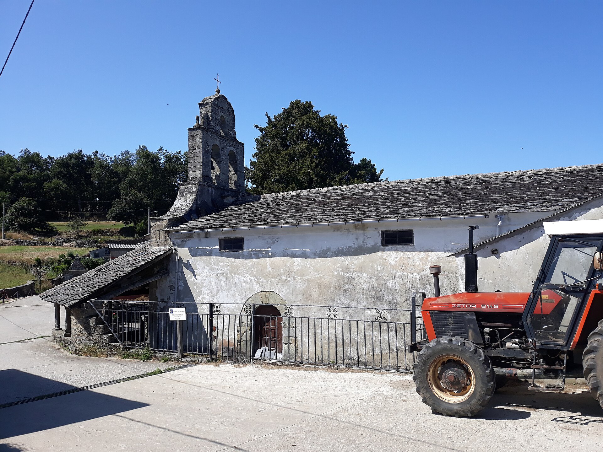 Un tractor estacionado frente a un edificio de piedra con campanario.