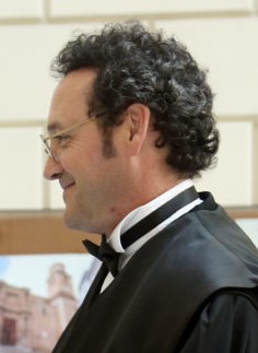 Un hombre con gafas y toga negra, visto de perfil.
