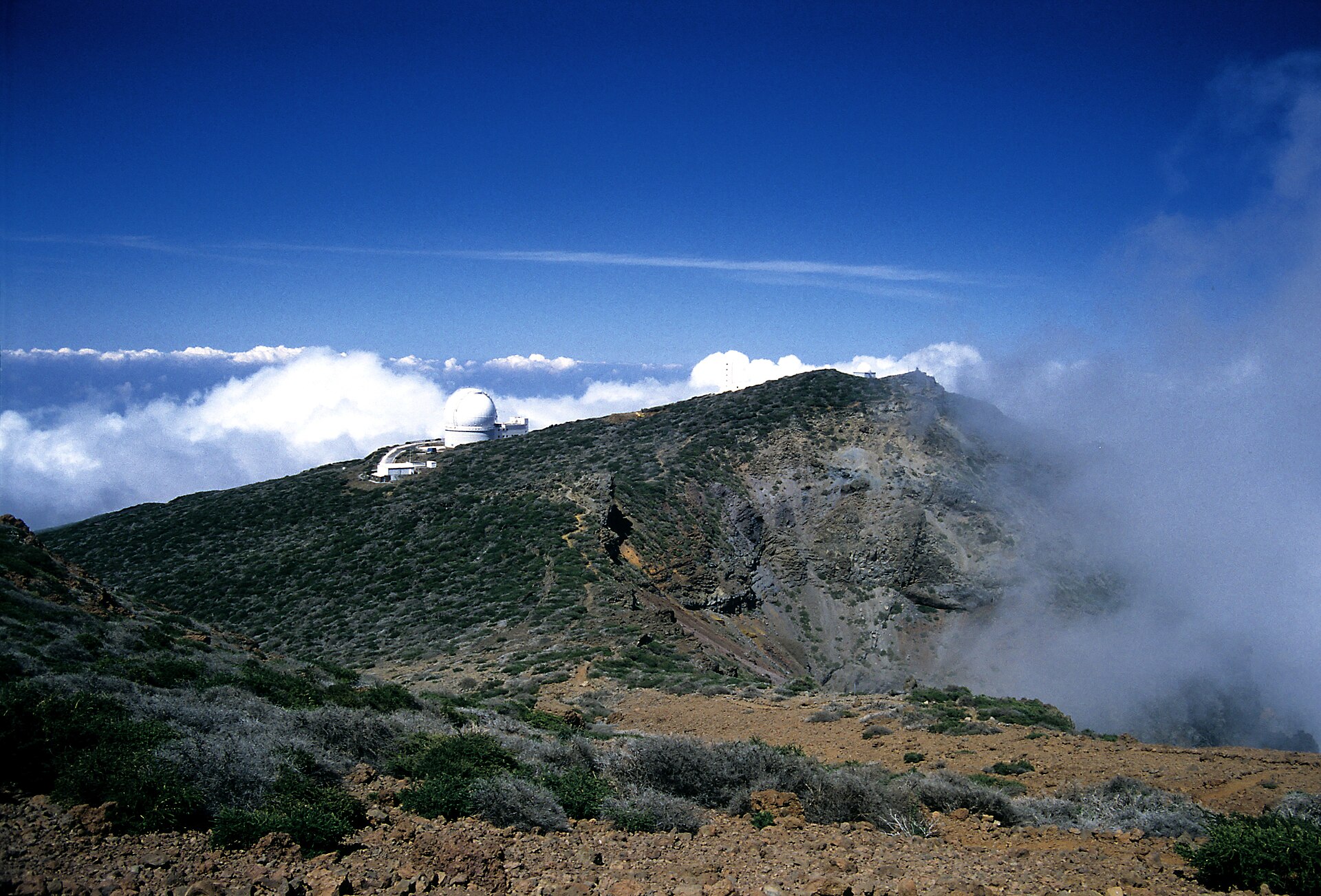 Una cúpula de observatorio se alza sobre una ladera rocosa cubierta de nubes.