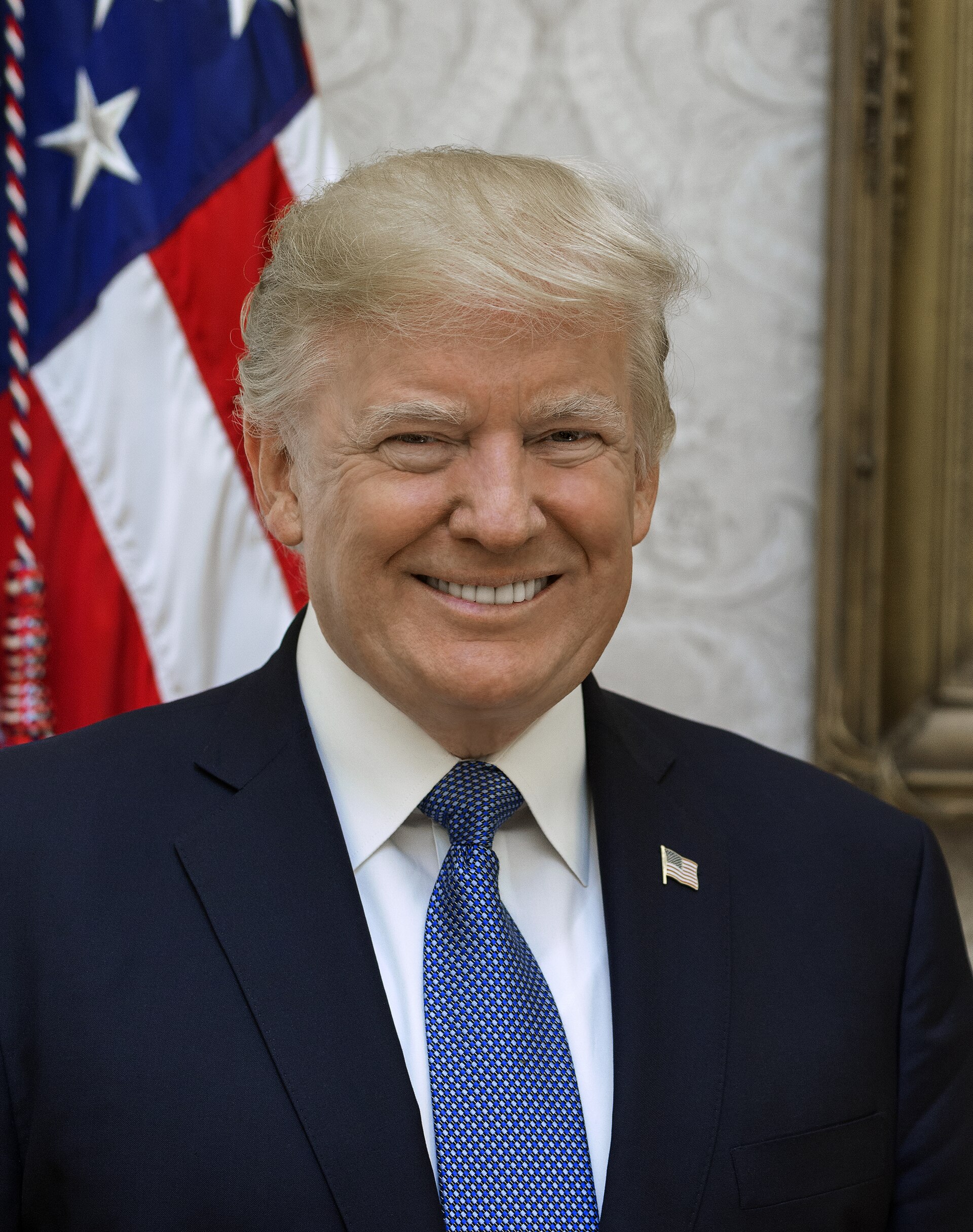 Retrato de un hombre sonriente con traje y corbata, ante una bandera de Estados Unidos.