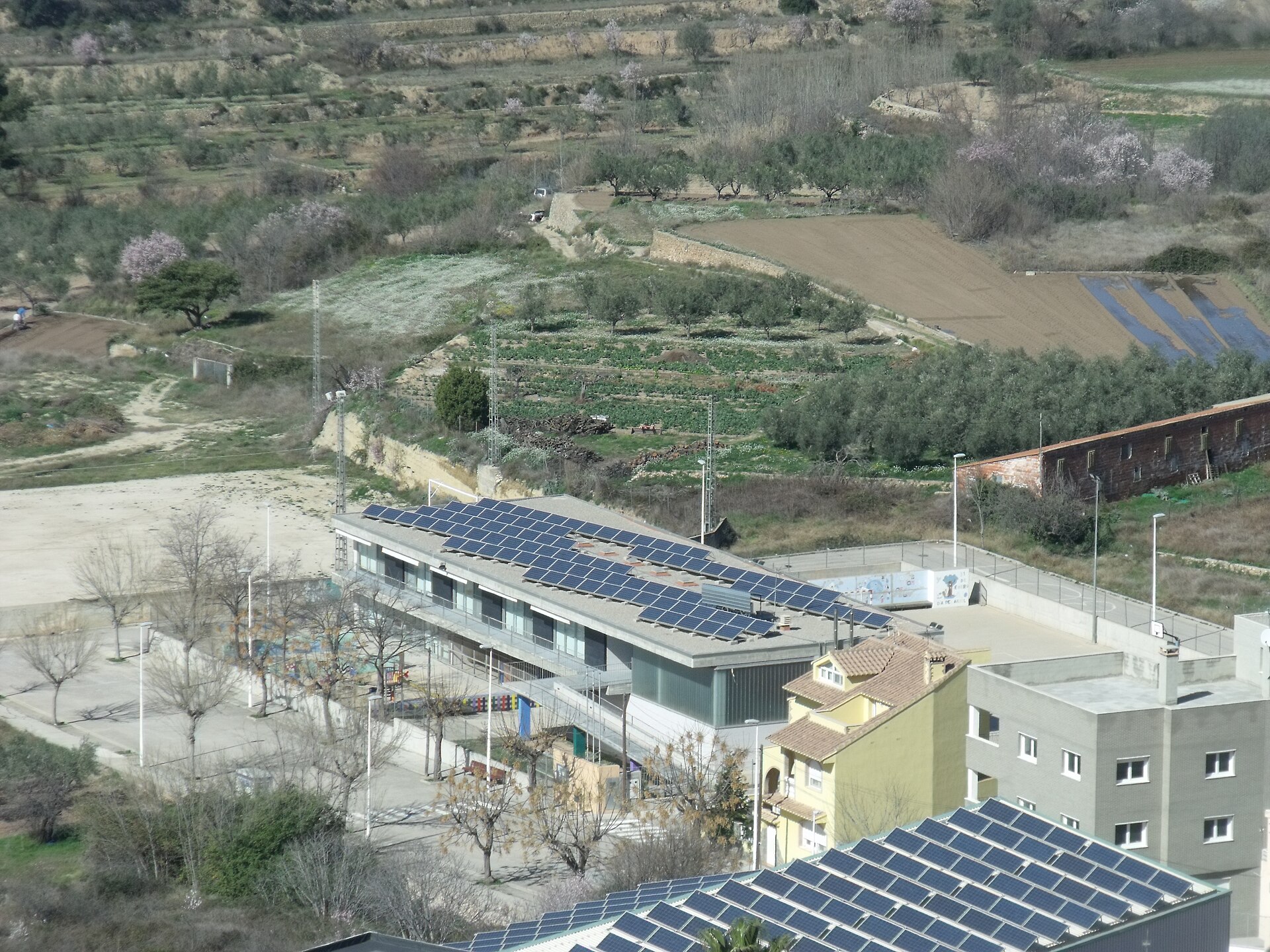 Vista elevada de un área con cultivos, viviendas y un edificio con paneles solares.