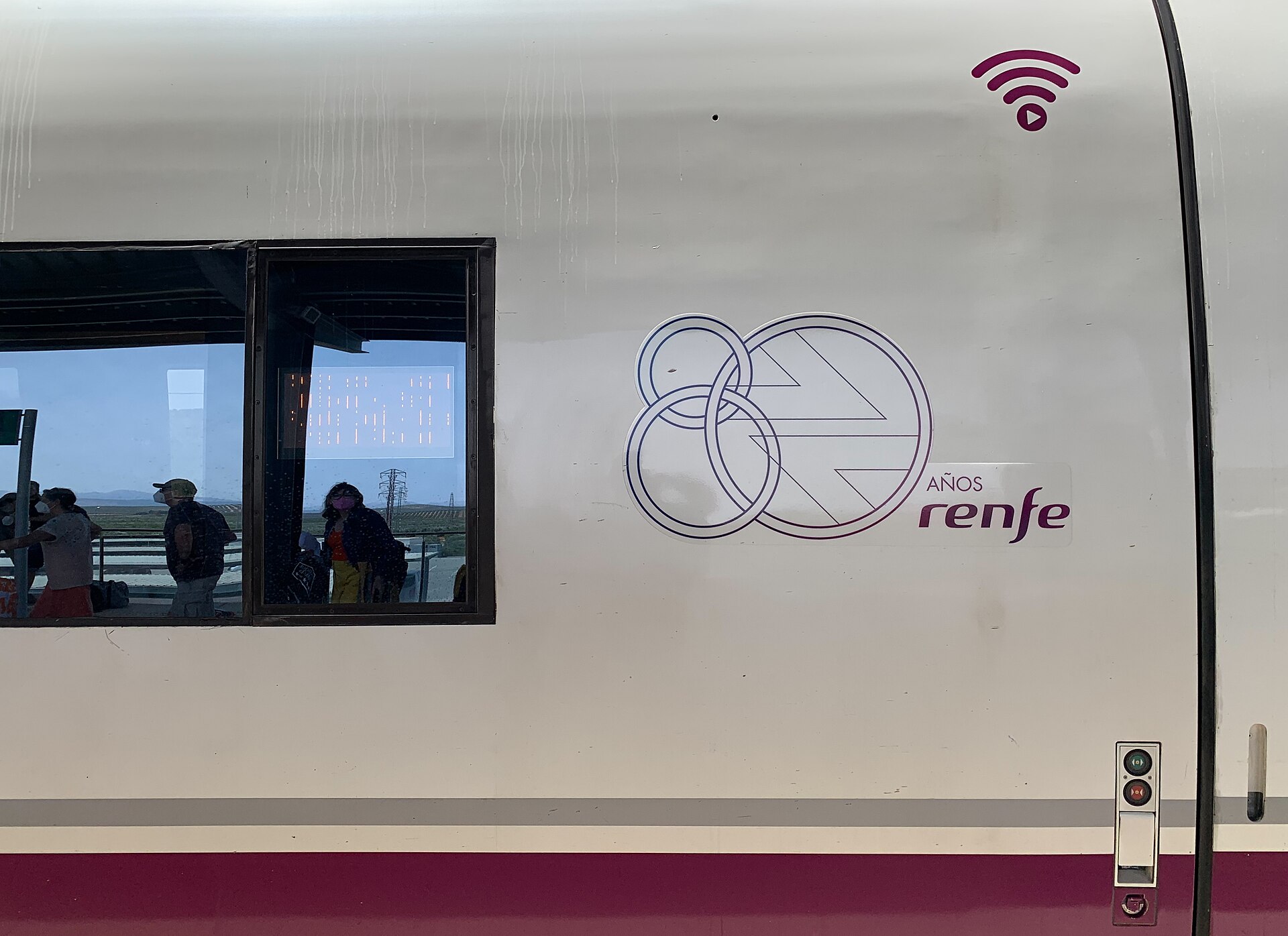 Detalle del lateral de un tren con el emblema de Renfe y una ventana con pasajeros.