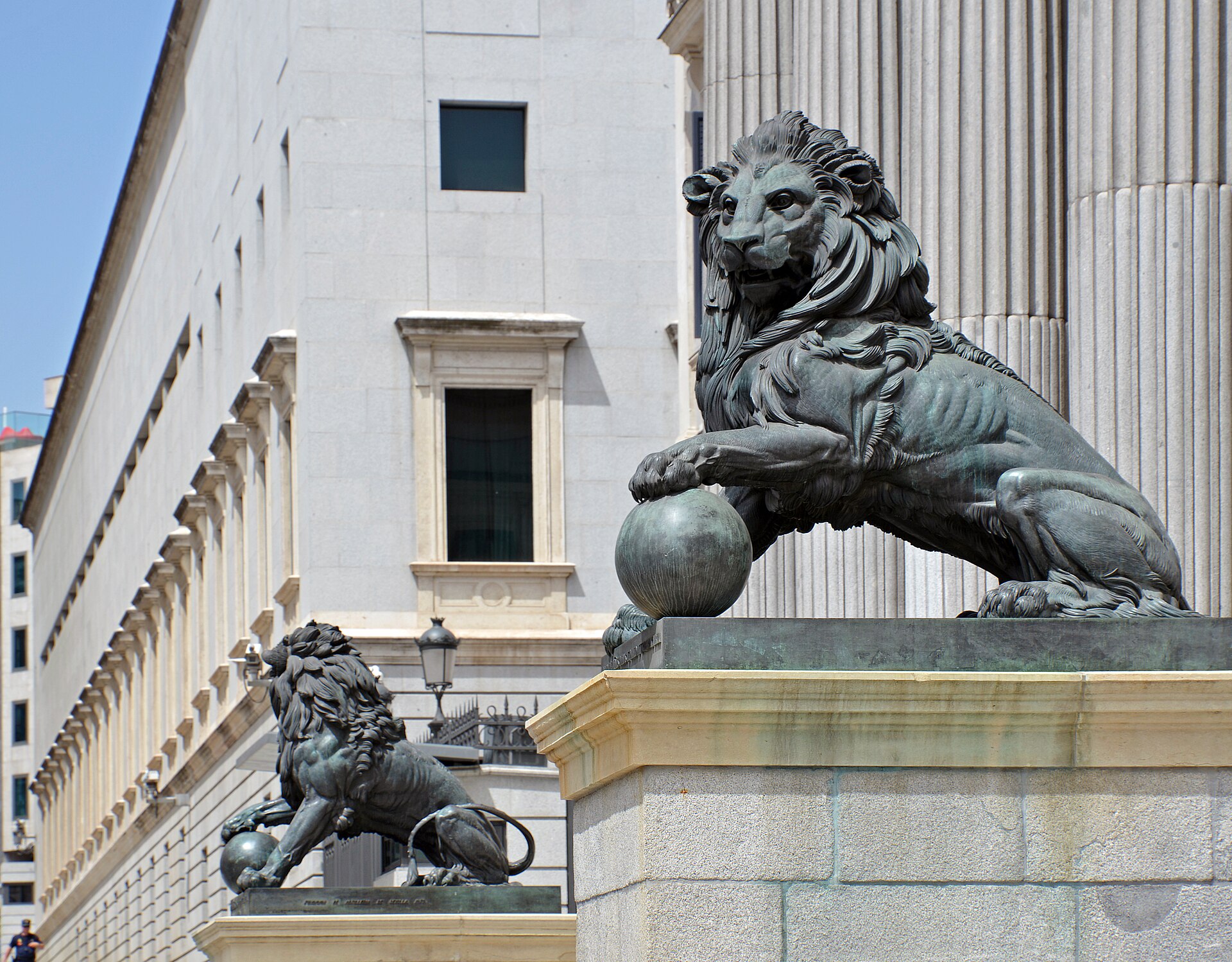 Escultura de un león ante una fachada de columnas.