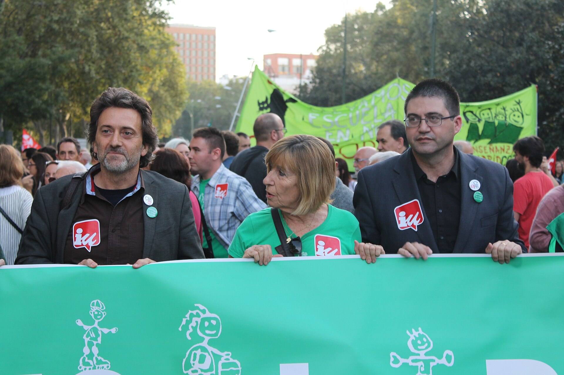 Personas sujetan una pancarta verde mientras otras avanzan entre banderas y carteles sobre educación pública.