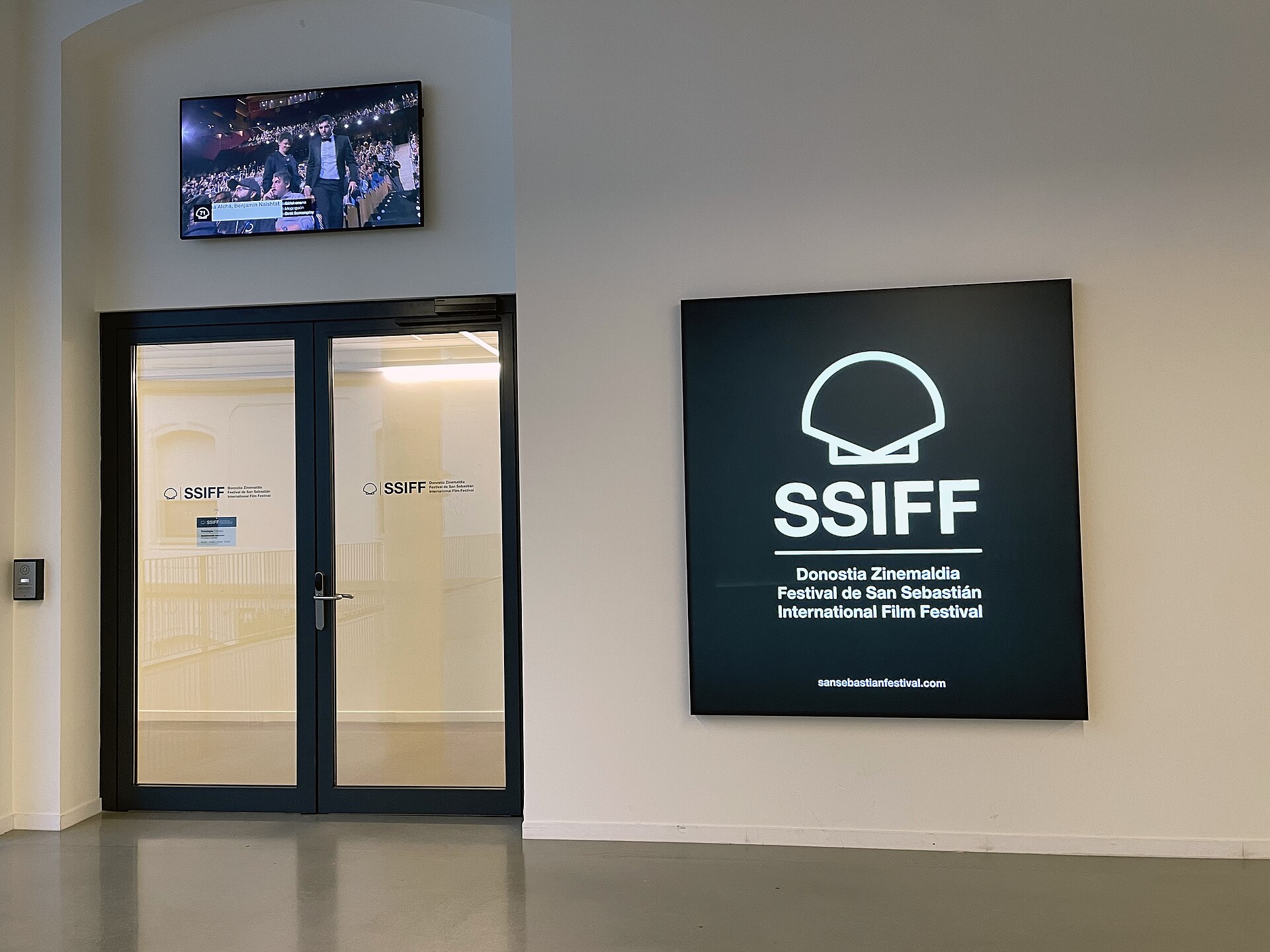 Entrada de unas oficinas con el logotipo del Festival de San Sebastián en una puerta y un panel.