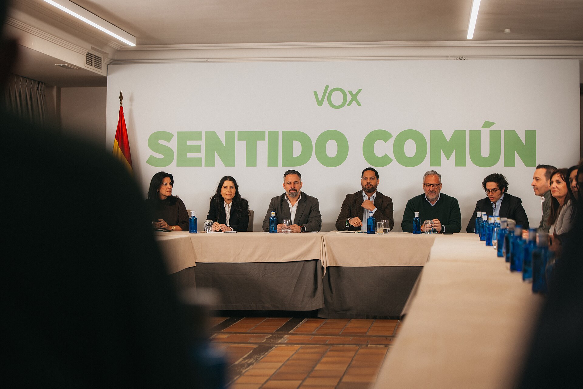 Varias personas sentadas a una mesa bajo un rótulo de Vox.