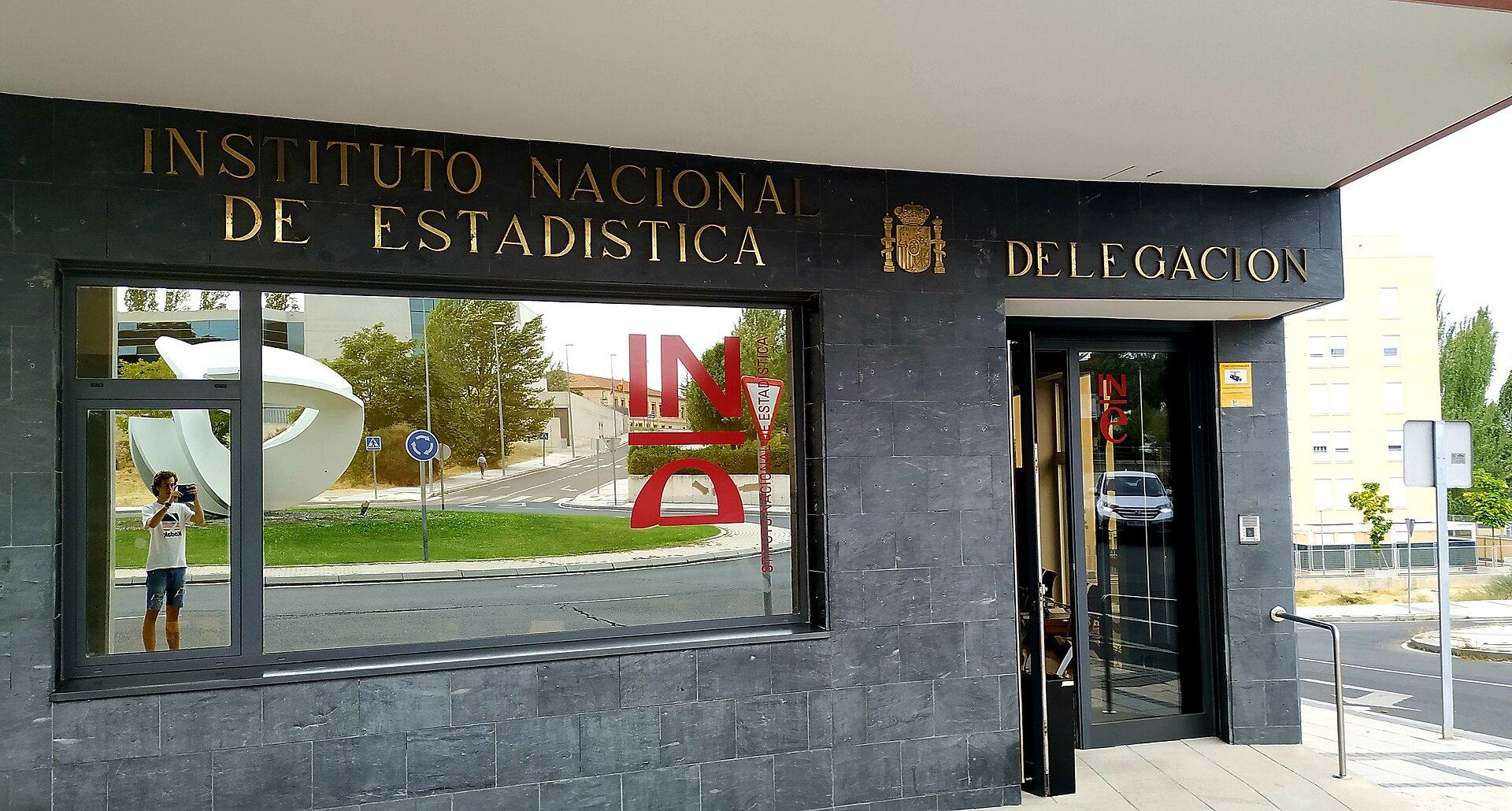 Entrada acristalada con el nombre de una institución sobre la fachada.