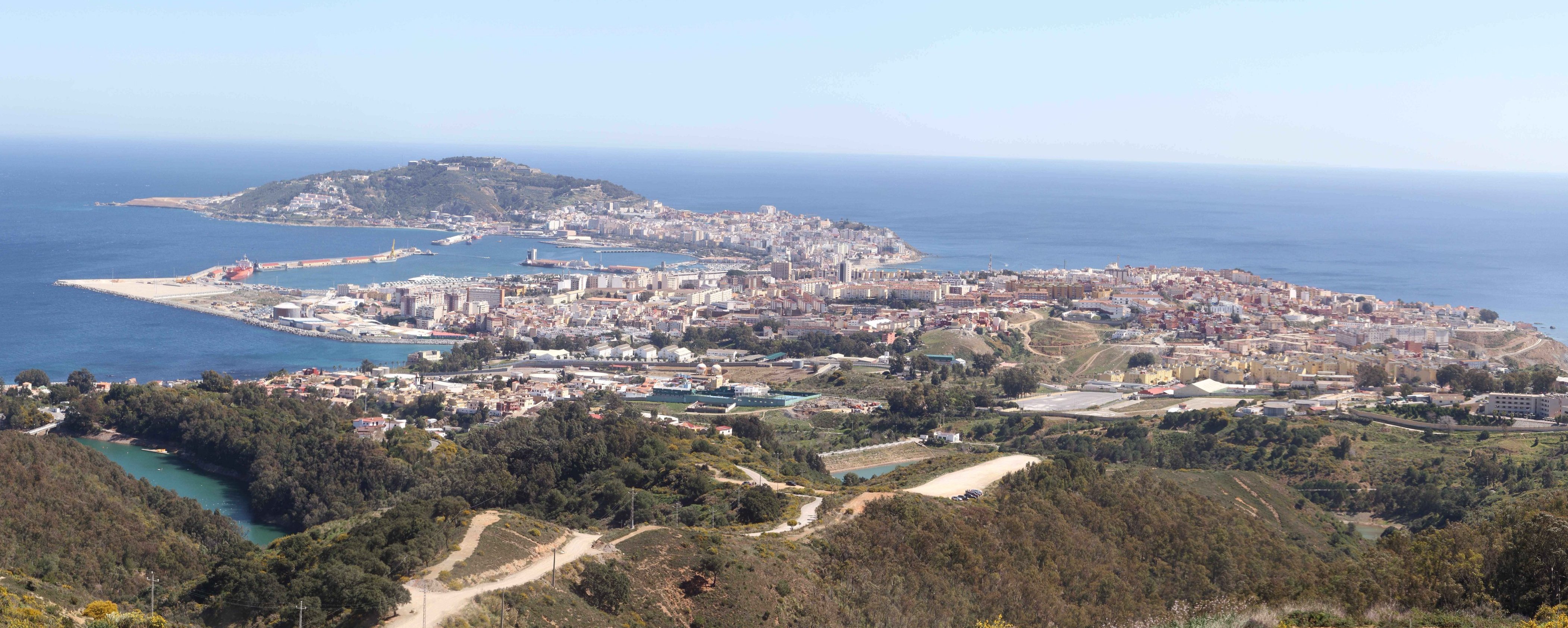 Vista panorámica de una ciudad costera extendida entre el mar, el puerto y una zona de colinas.